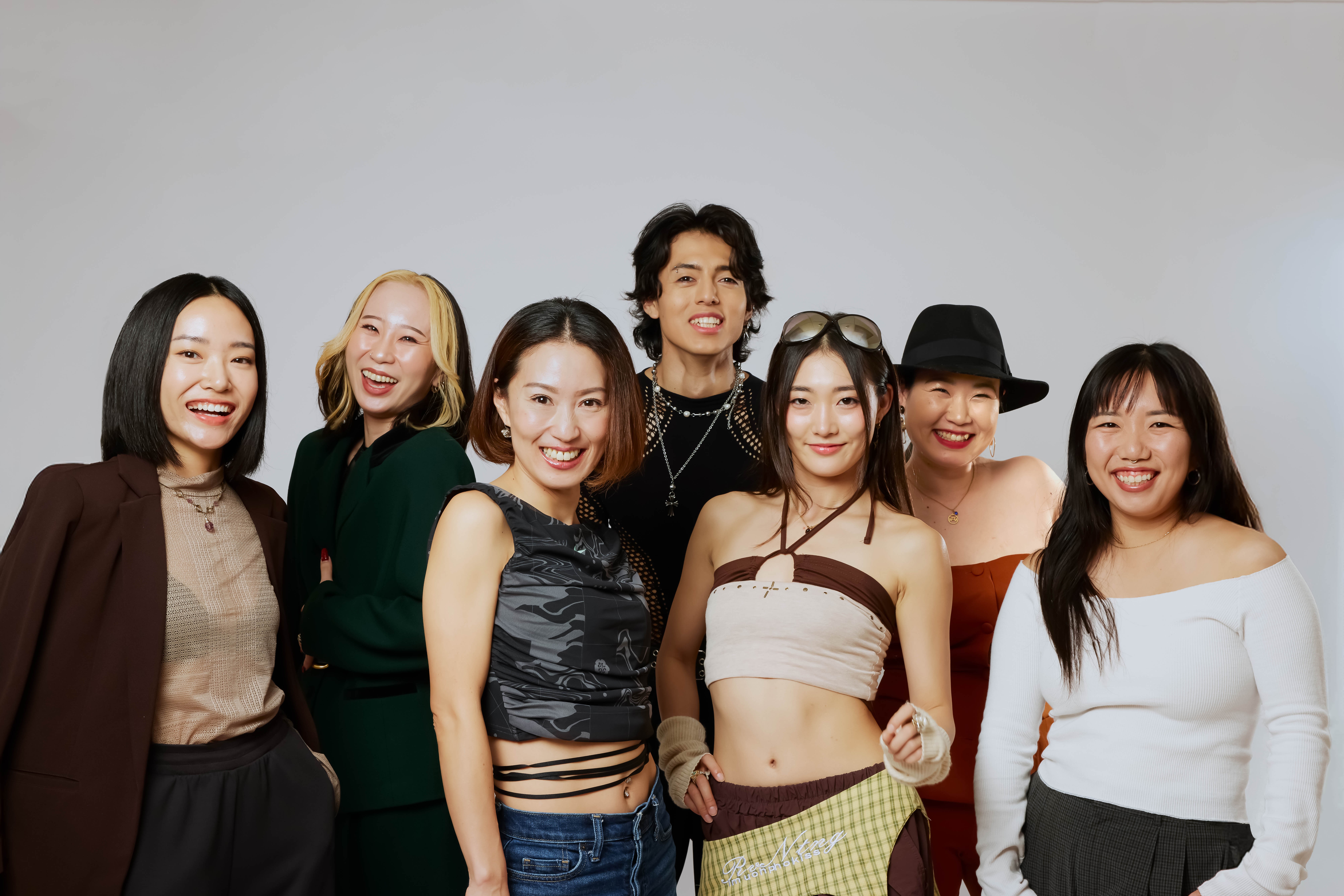 Group of seven women smiling, standing together against a plain background.