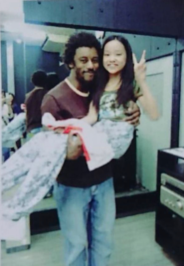 Man holding a wrapped gift with a girl making a peace sign, both smiling indoors.