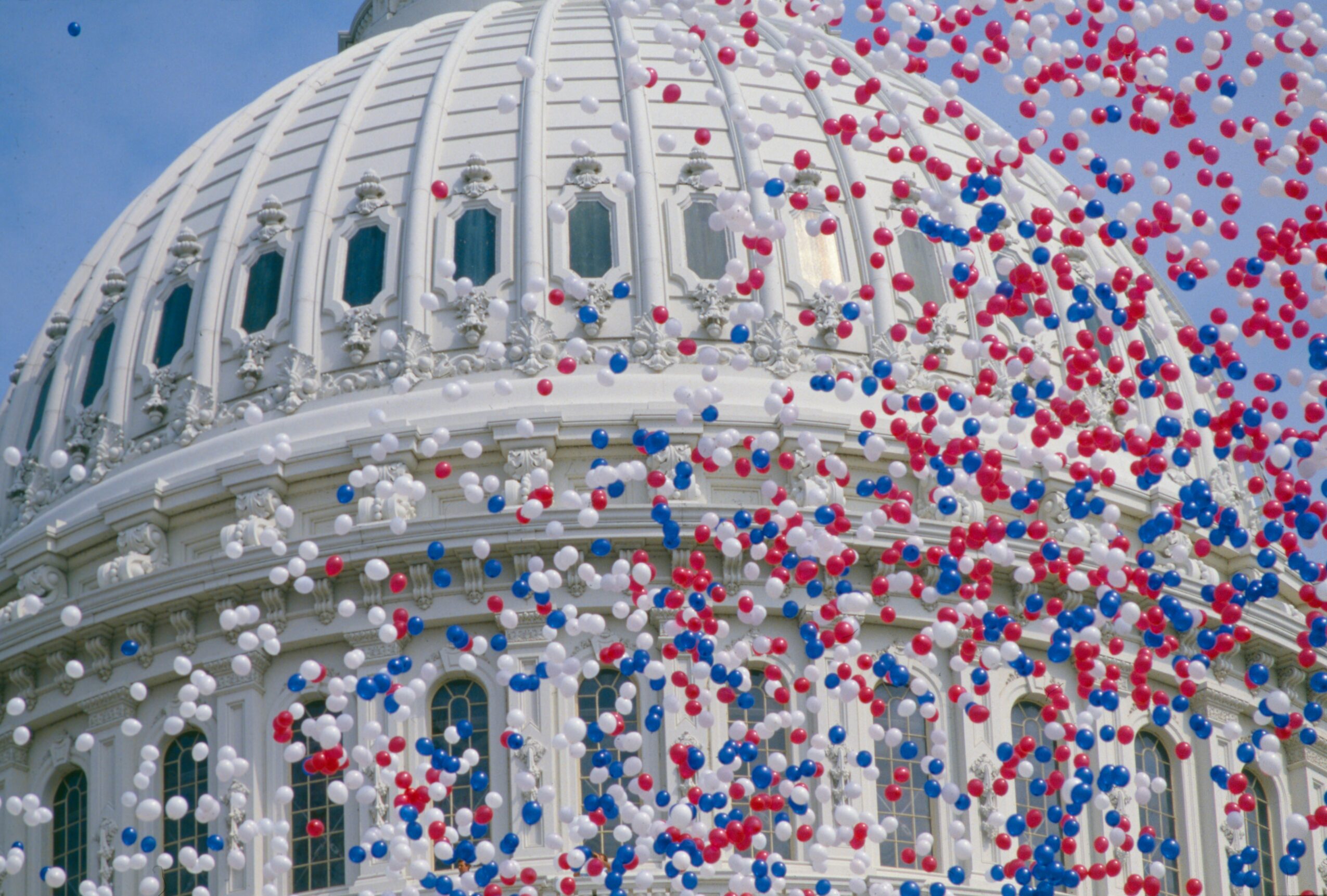 Balloon release in front of a domed government building with ornate architecture, blue sky background.