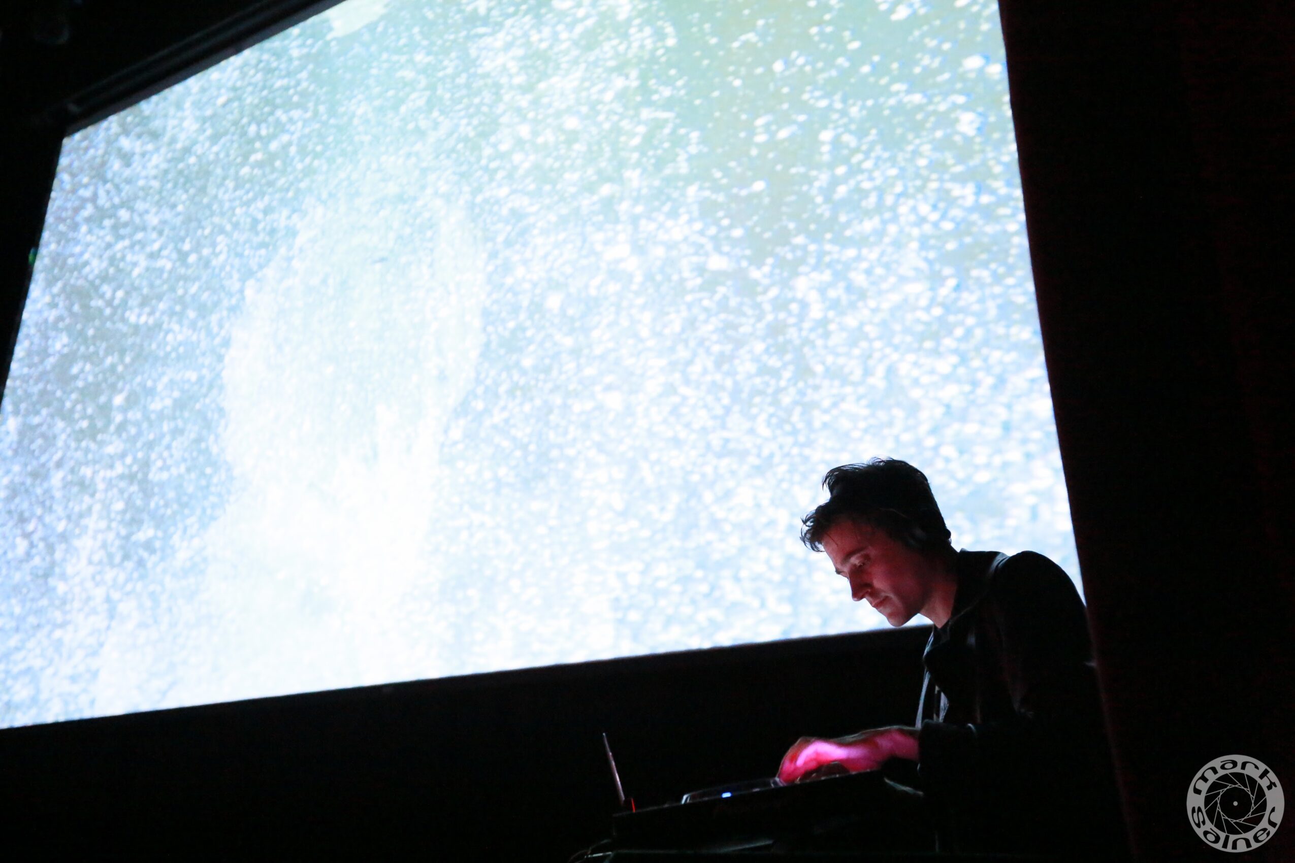 Person working on a laptop in front of a large screen displaying a blue and white abstract pattern, silhouette visible.