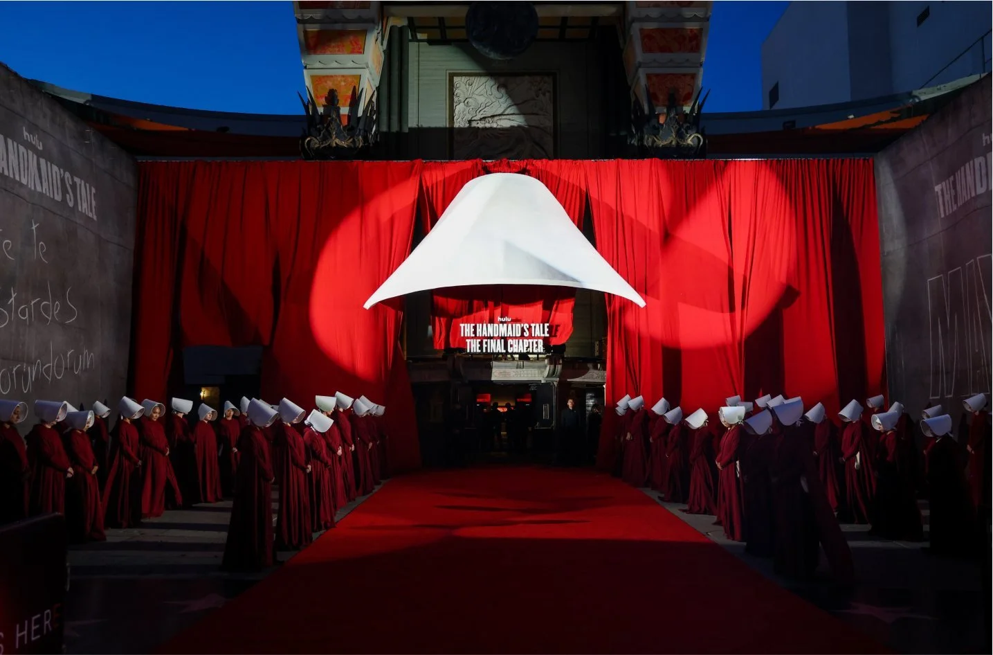 Stage with red curtains, a white lampshade hanging, and chairs with white covers, set for an event.