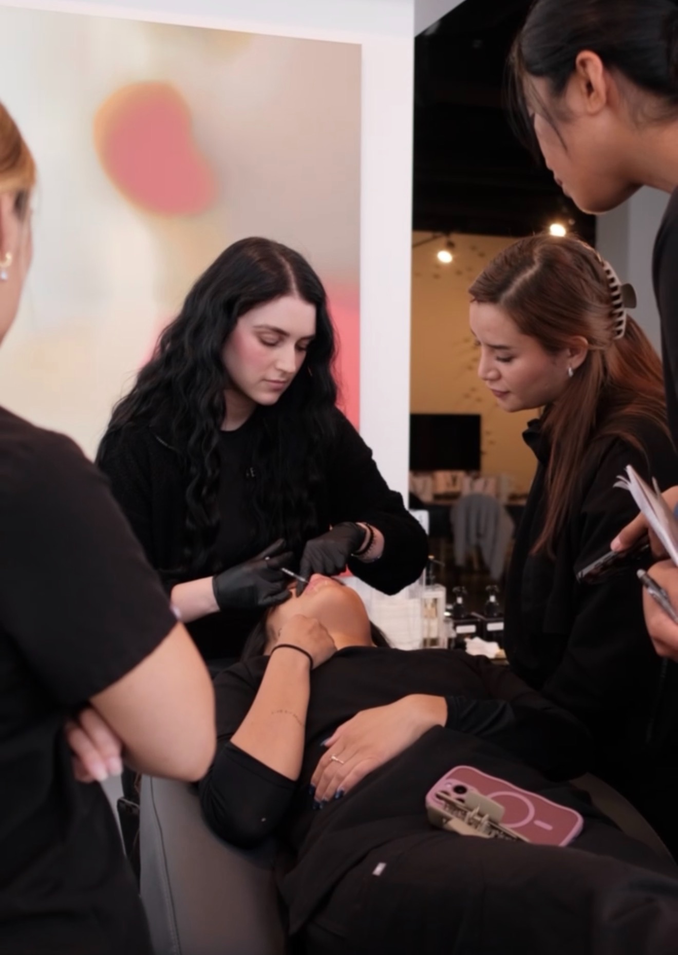 A group of women, one with black hair and gloves, performs a procedure on a person lying down in a professional setting.