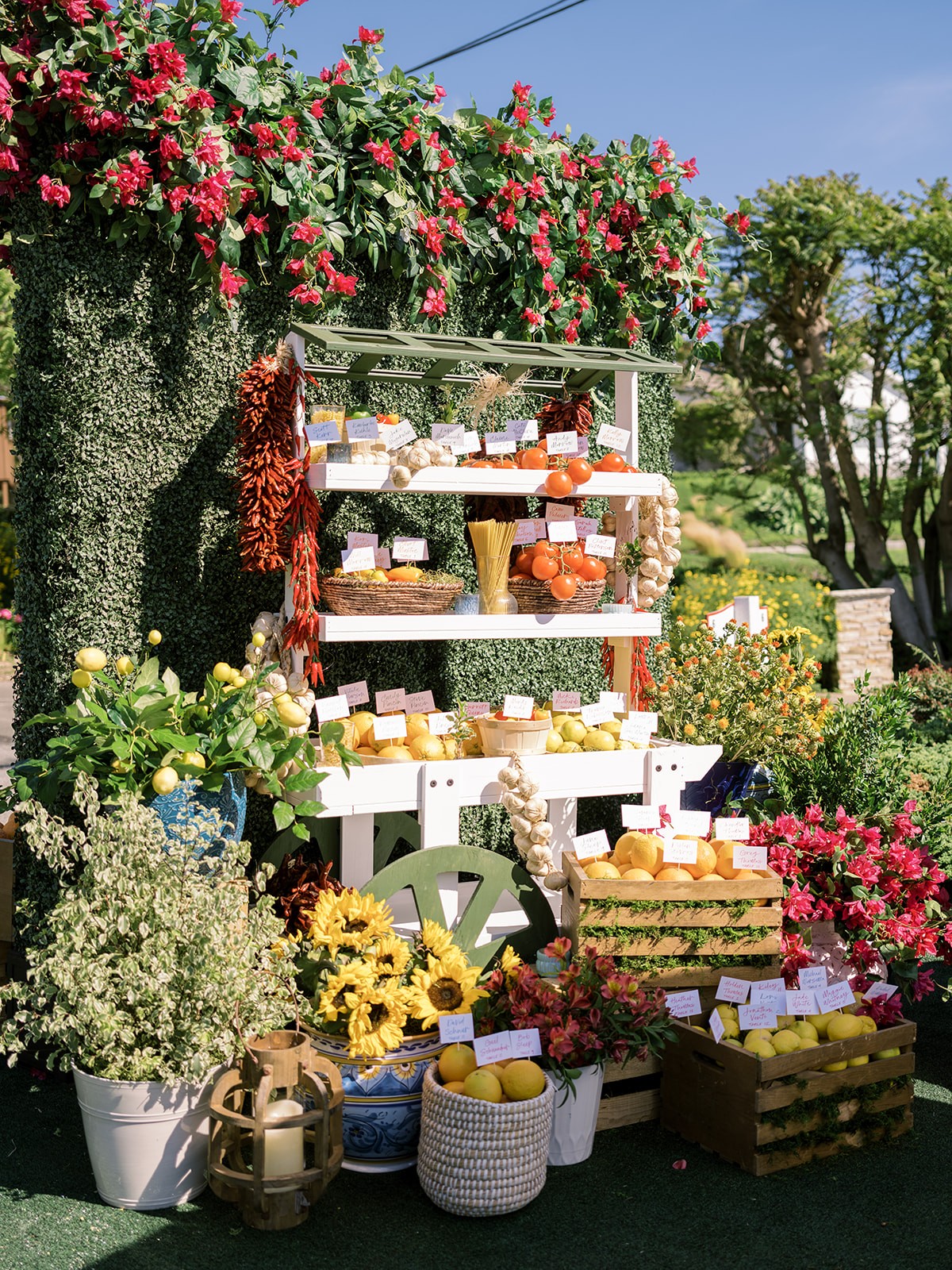 Display of soap and bath products on shelves outdoors, surrounded by colorful flowers and greenery, under a clear sky.