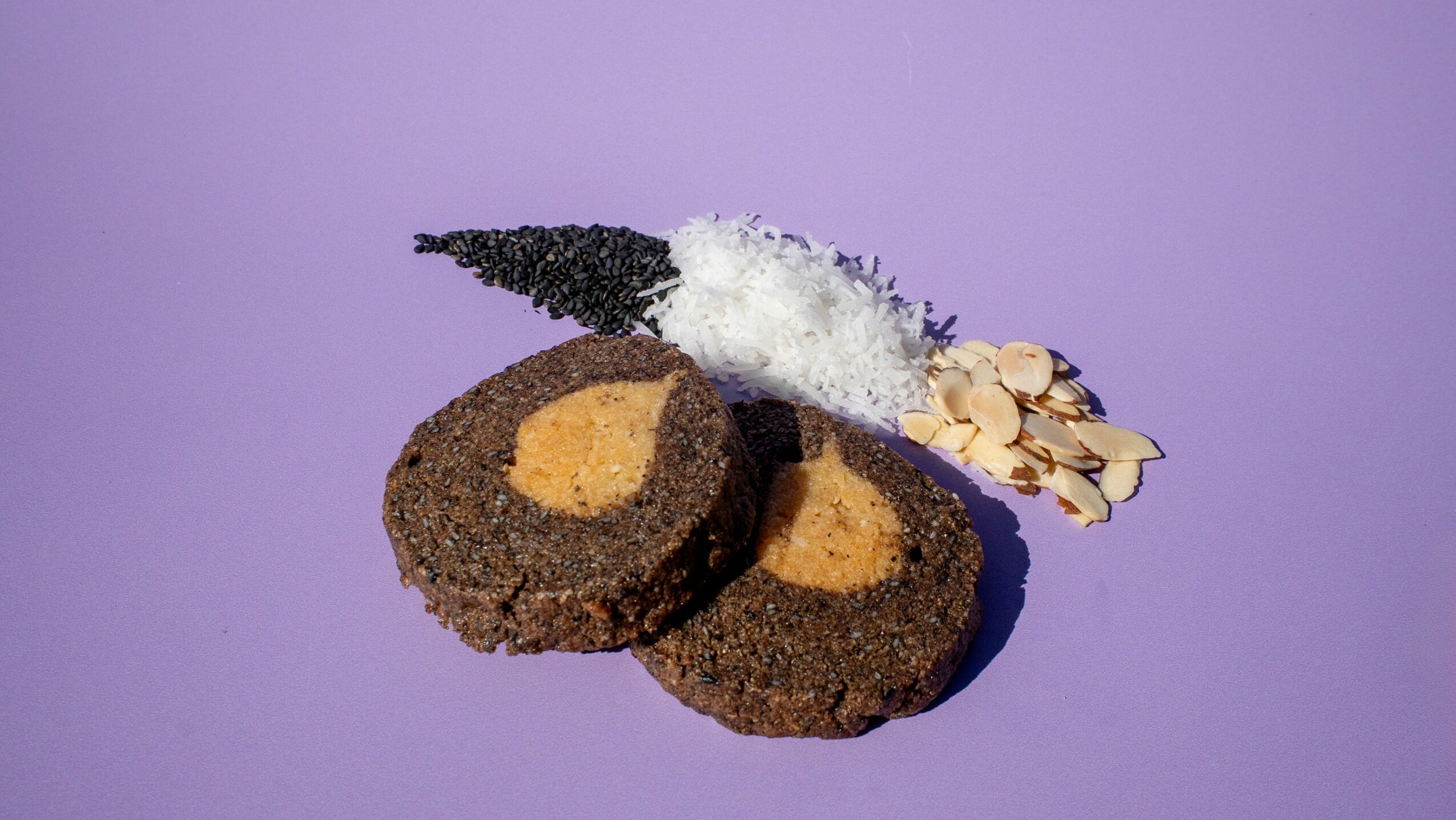 Two cookies with almond slices and a decorative leaf on a purple background.