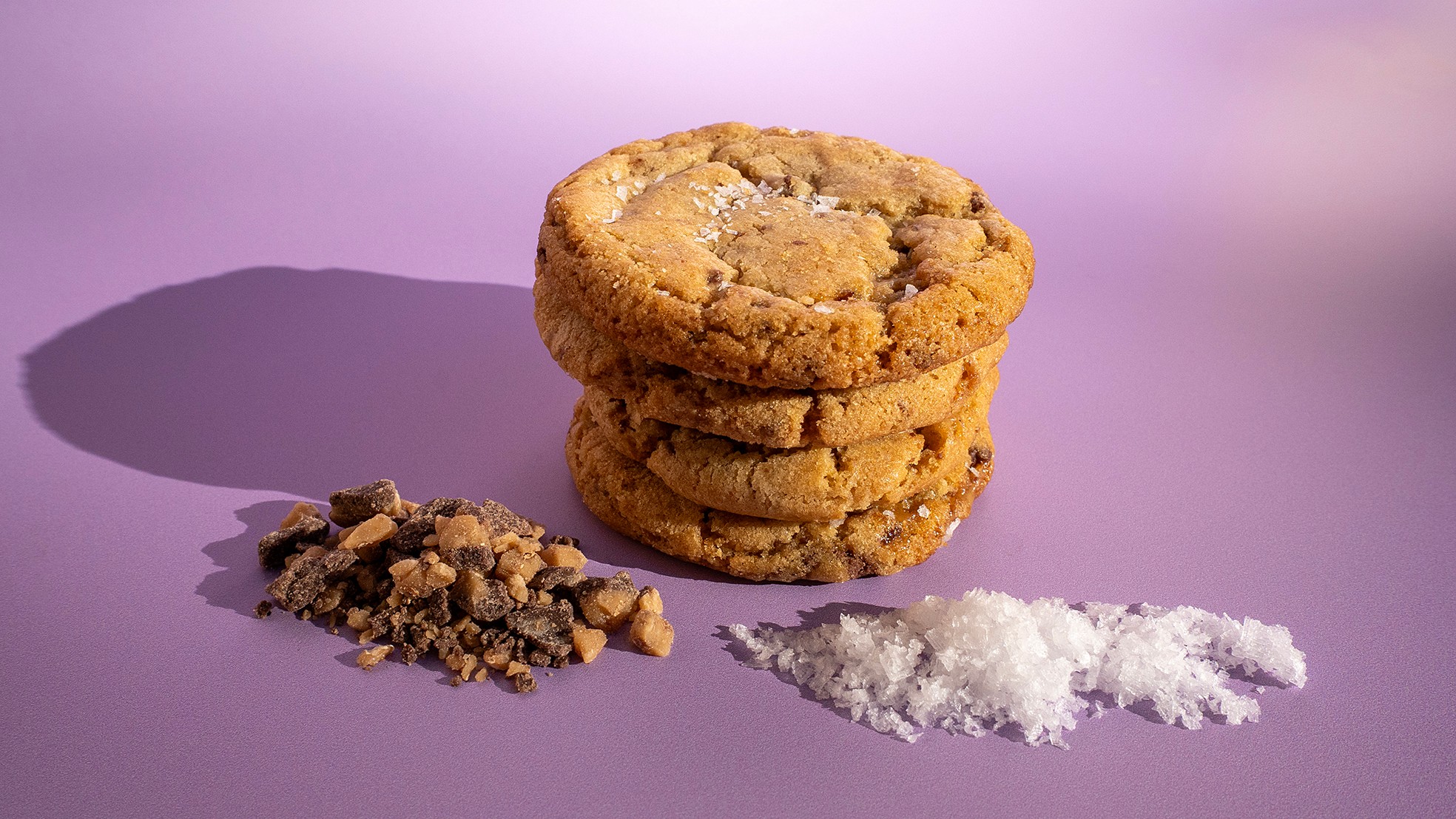 Stack of three cookies, with crushed cookie and white powder on purple surface, shadow cast to the left.