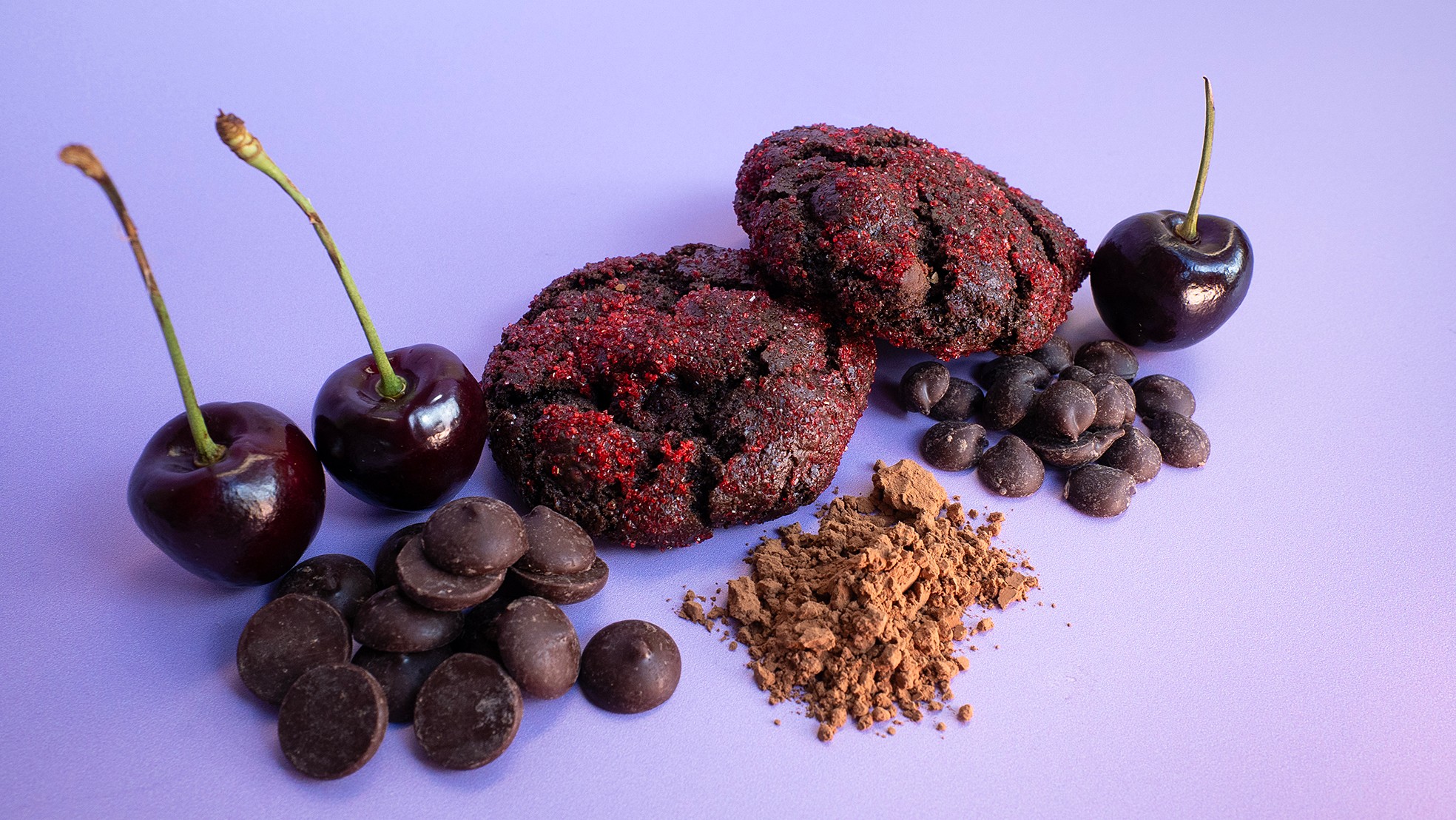 Three blackberries, cherries, chocolate candies, and brown sugar on a light purple background.