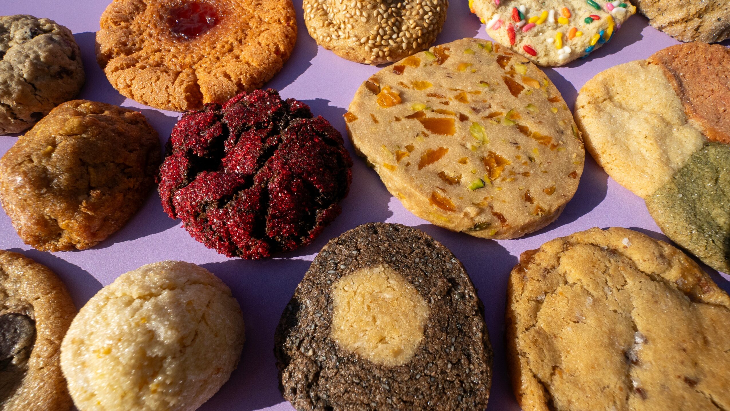 Assorted cookies with various shapes, colors, and textures on a purple surface.