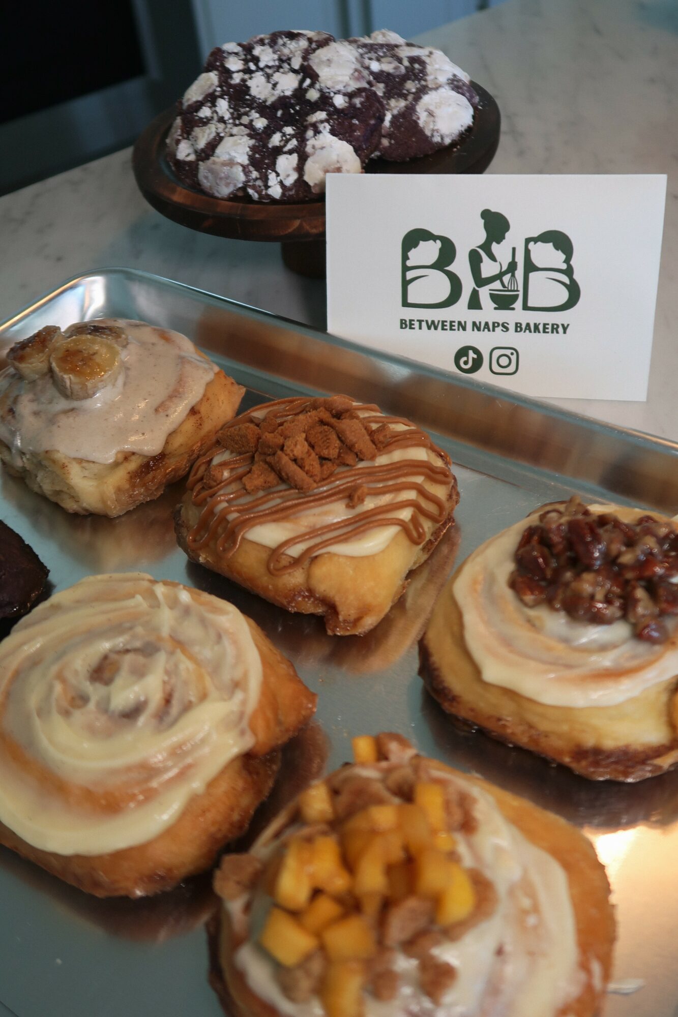Assorted baked goods on a tray with a bakery card, including cookies and pastries with toppings and fillings.
