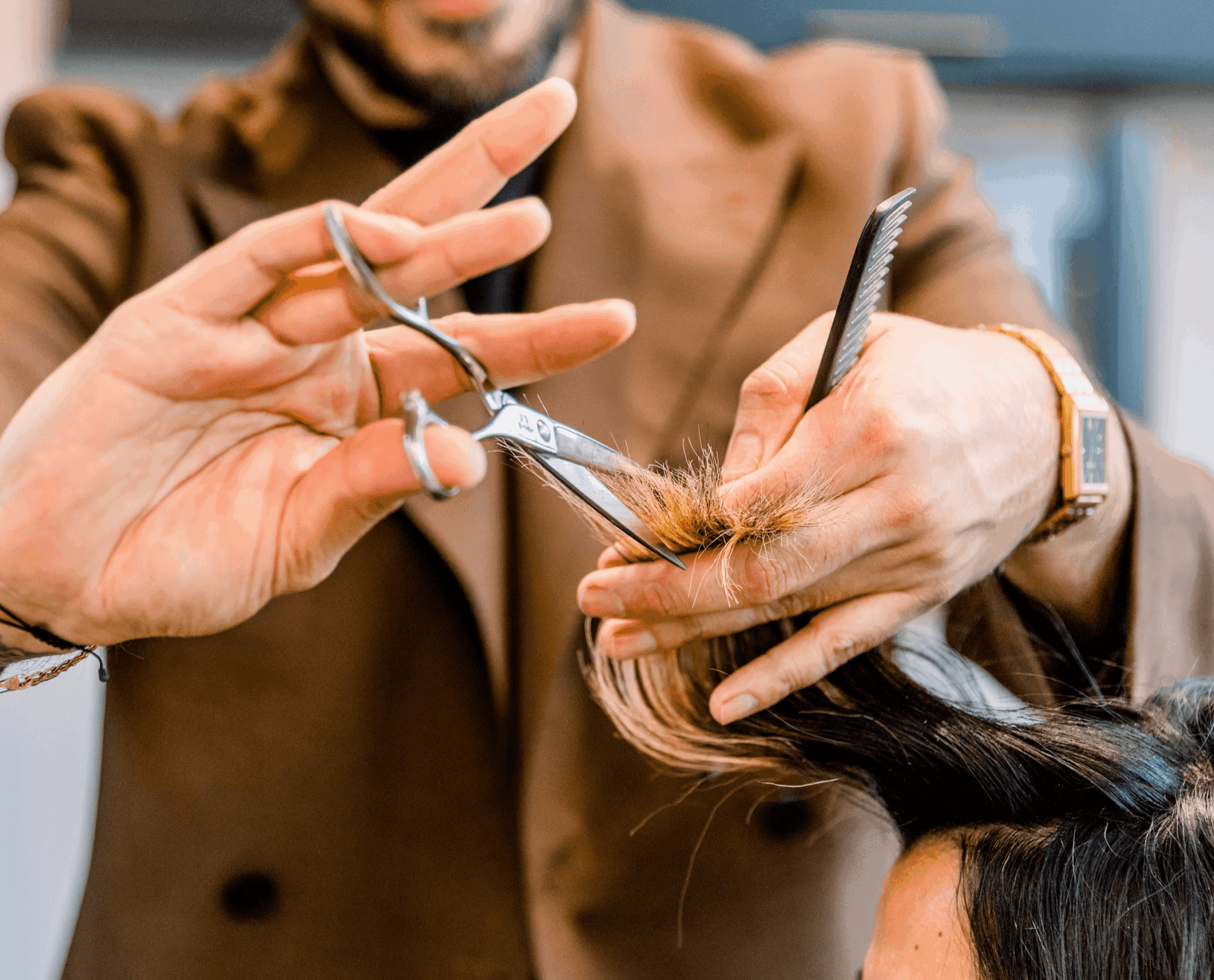Person holding scissors and comb trimming a person's hair in a salon, with a blurred background.