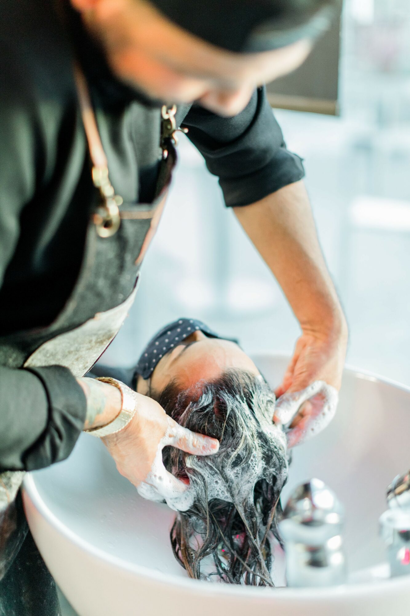Person washing a dog's hair in a sink, with soap lather and water, in a grooming setting.