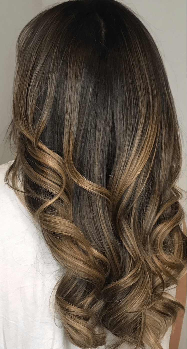 Back of a person's head with long, wavy, brown hair with lighter highlights.