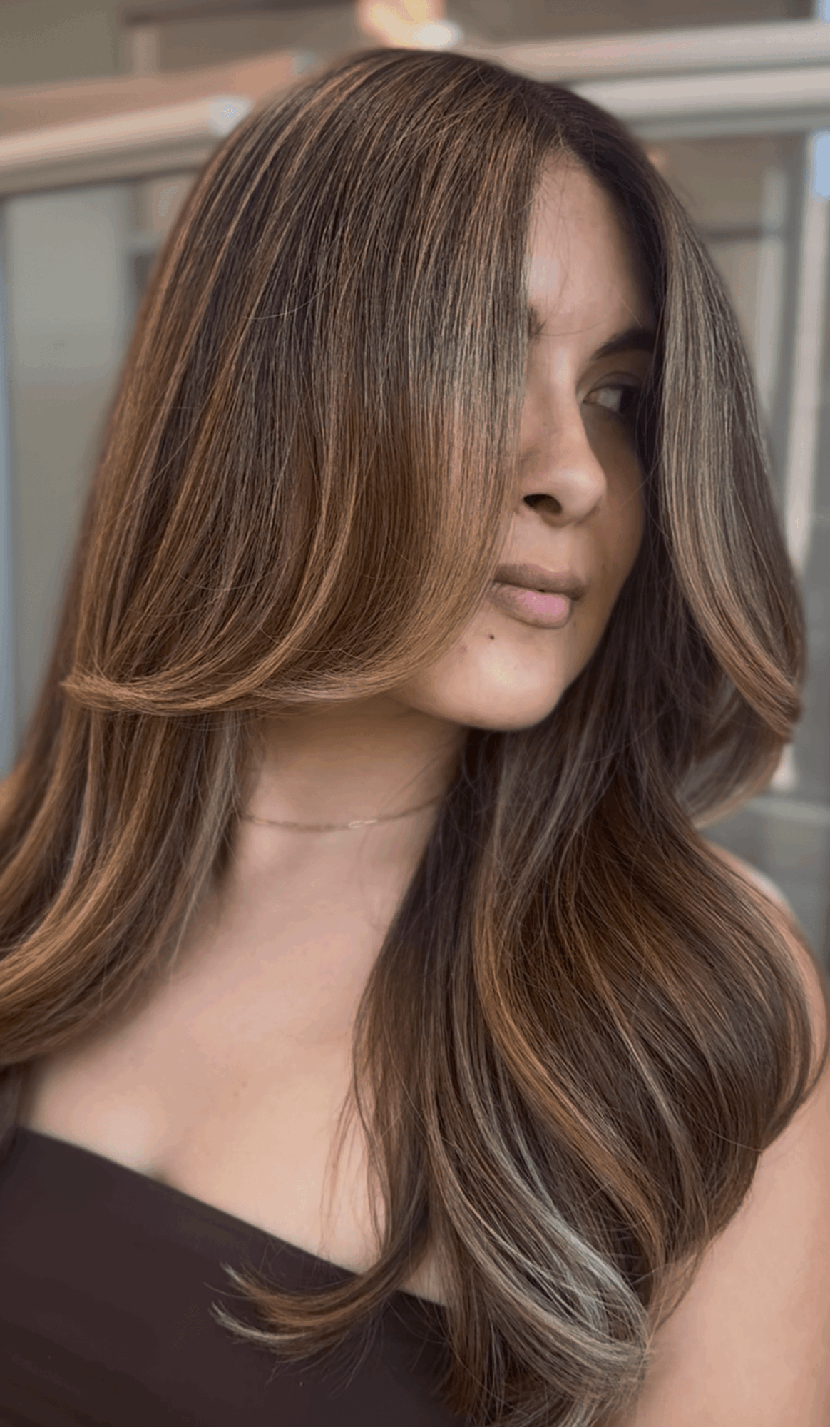 Young woman with long, wavy hair and natural makeup, looking to the side indoors.