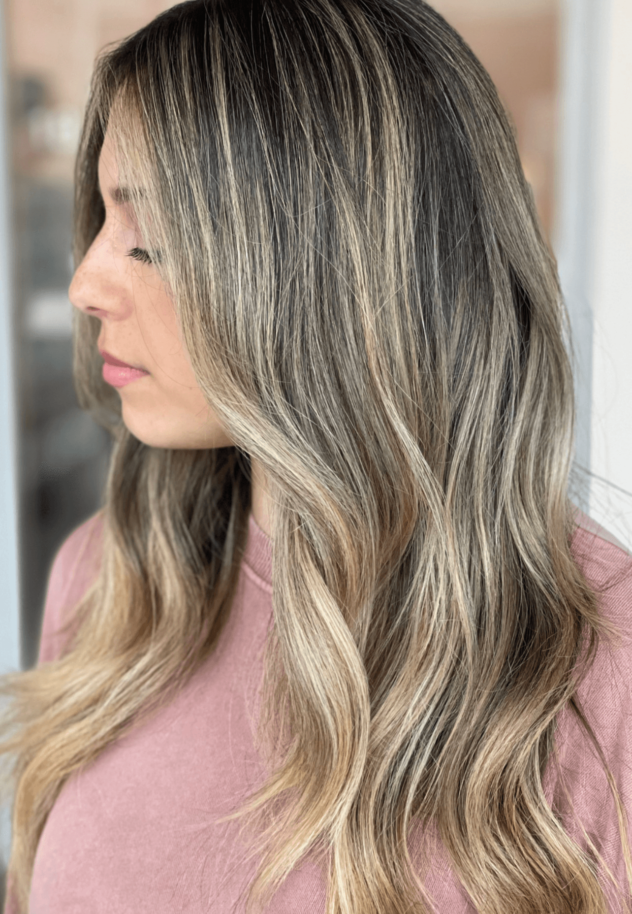 Side view of a woman with long, wavy, blonde hair and a pink top.