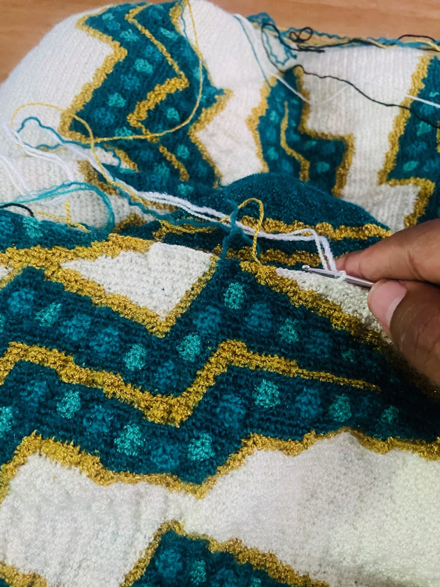 Close-up of a person knitting a colorful geometric patterned fabric with yarn and knitting needle, vibrant blue, yellow, and white colors.
