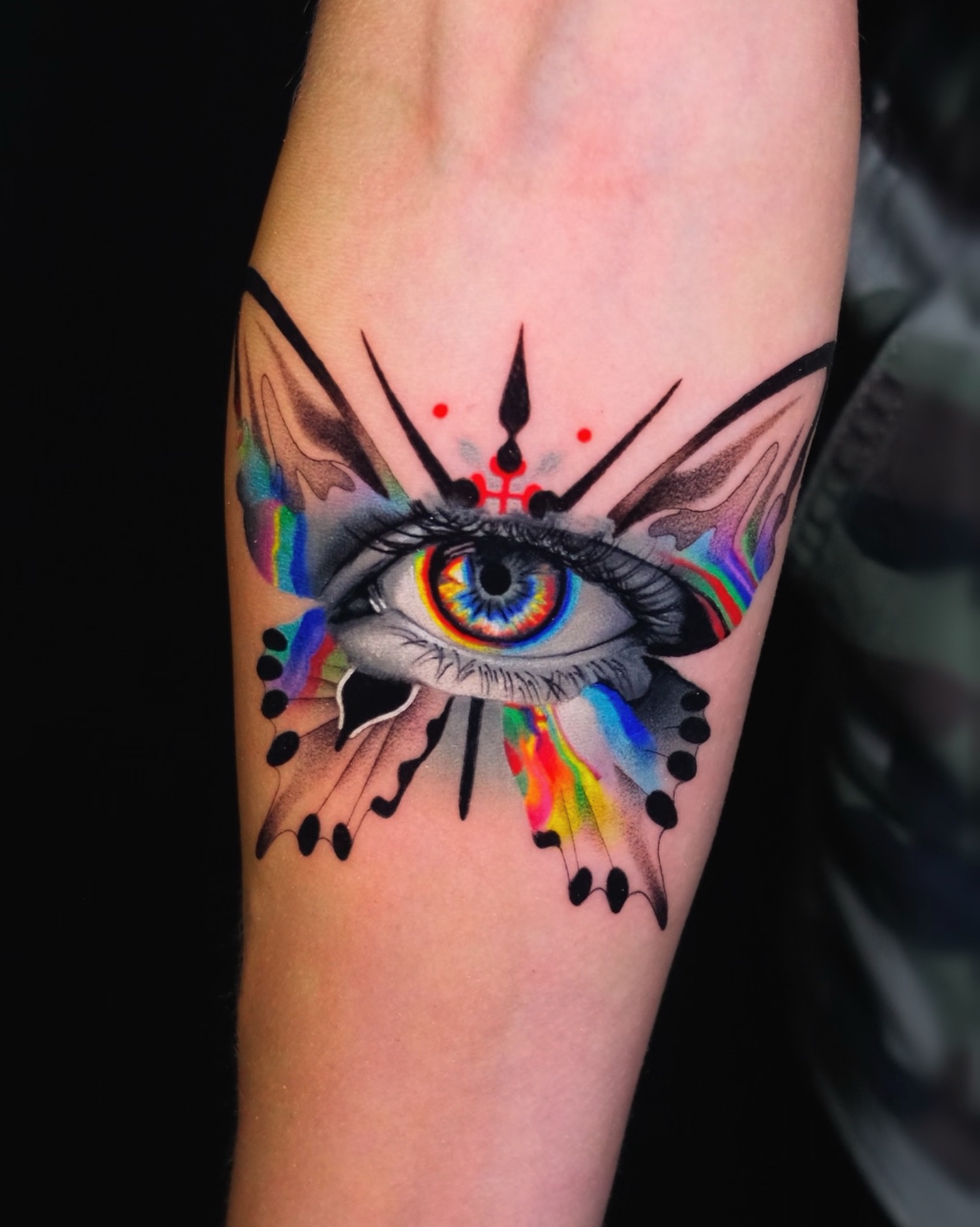 Tattoo of an eye with colorful details and abstract elements on skin.