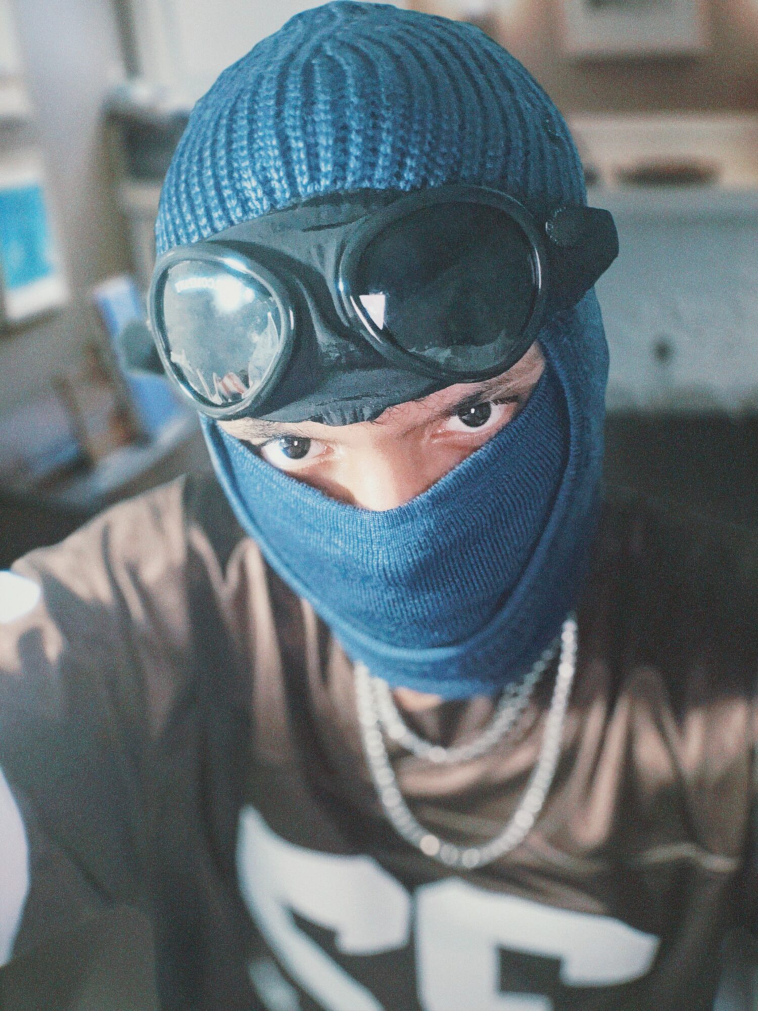 Person wearing a blue beanie, goggles, and a face covering, looking directly at the camera.