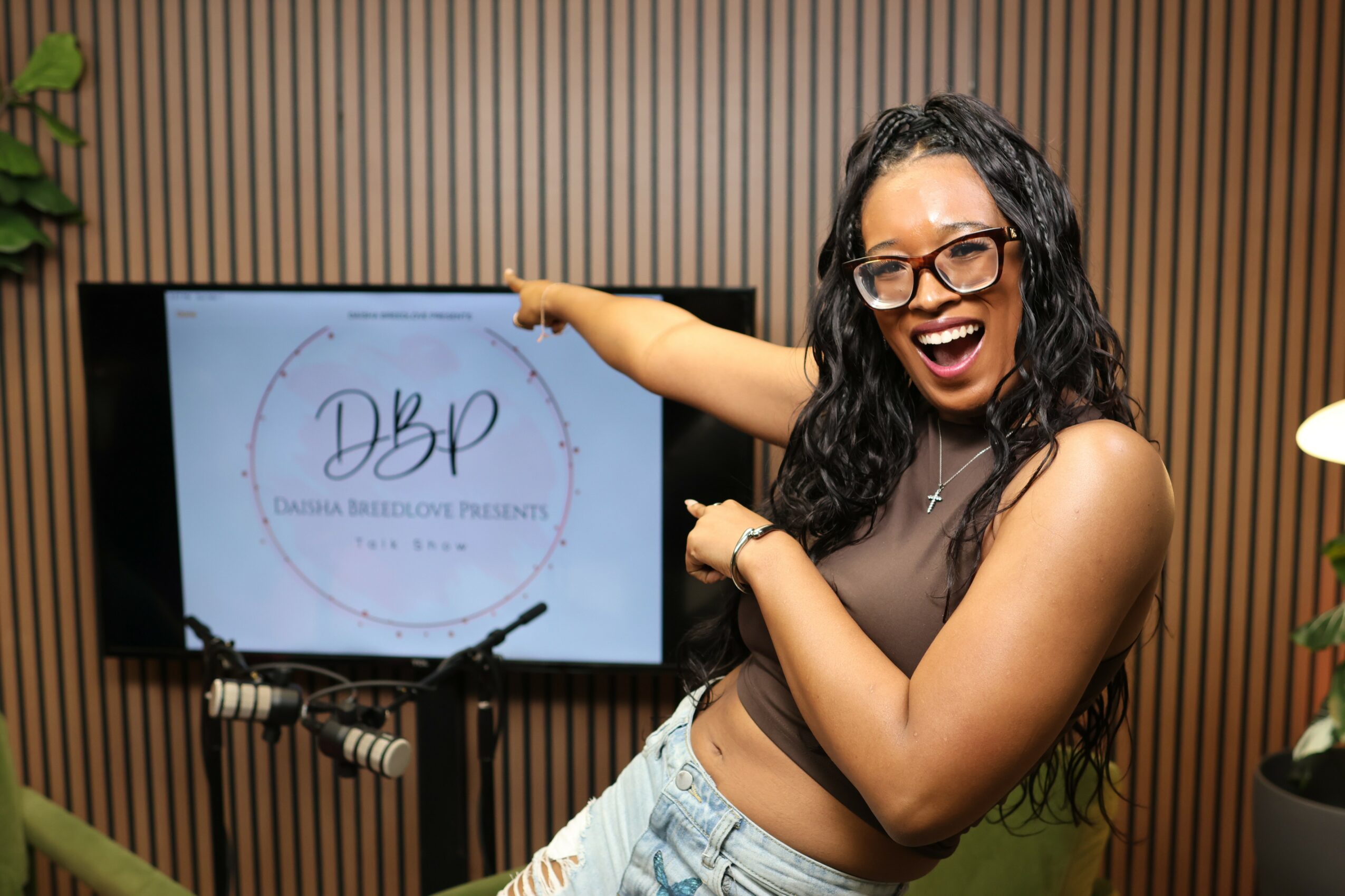 Woman with glasses smiling and pointing at a presentation screen in a room with wooden wall panels.