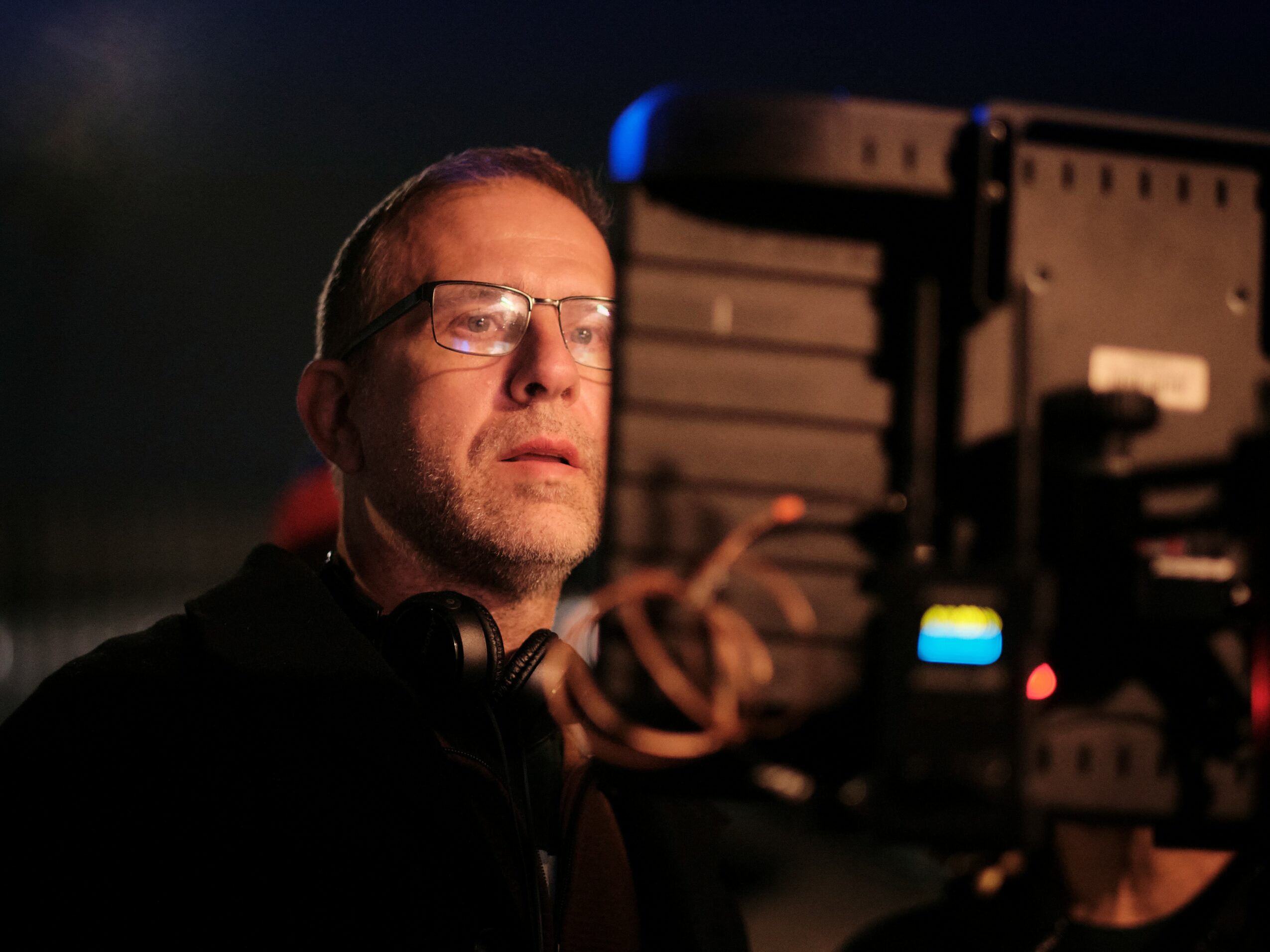 Man with glasses and headphones looks at a screen in a dark environment.