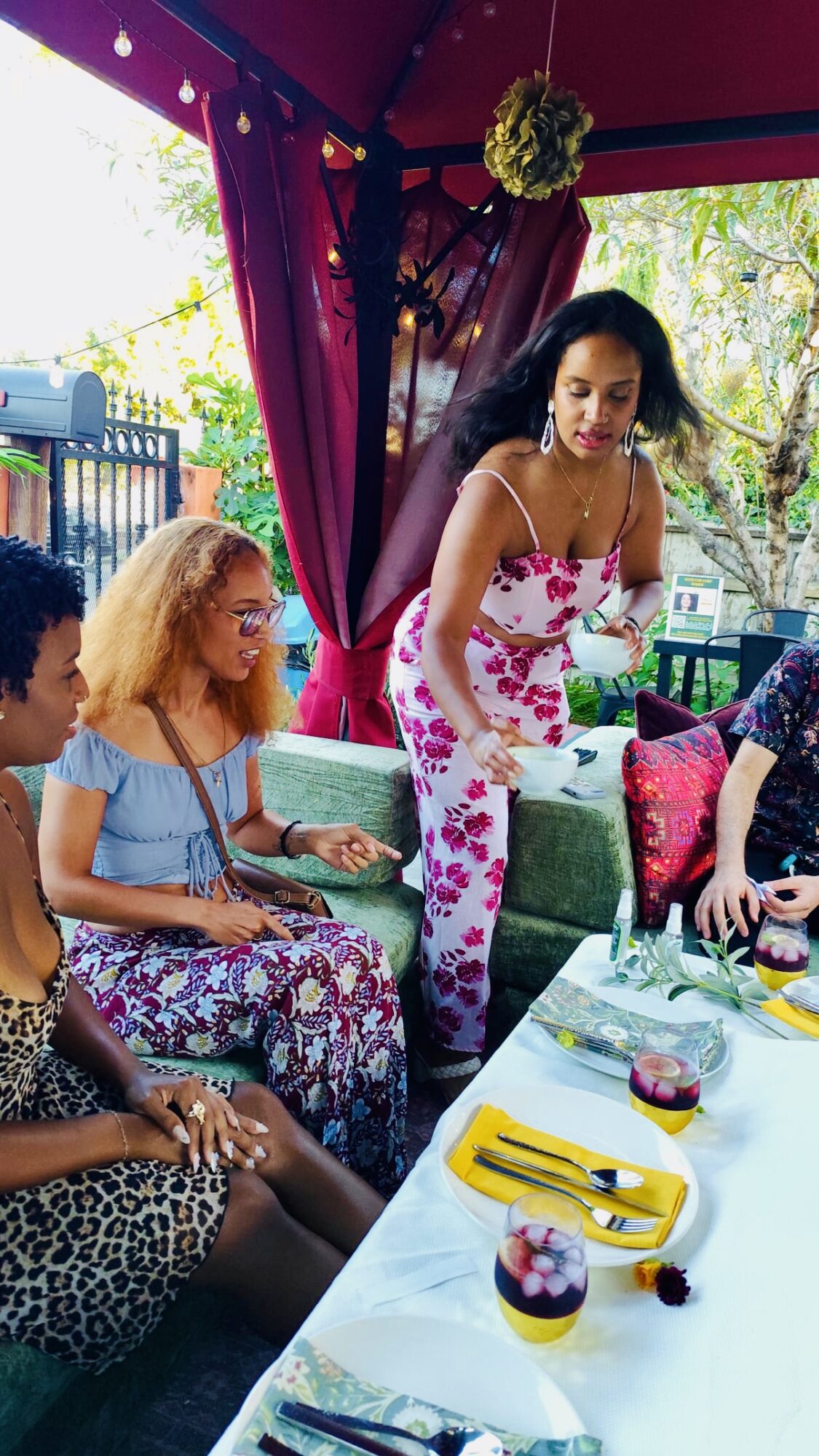 Group of women at a table outdoors, with colorful decorations and drinks, engaging in conversation.