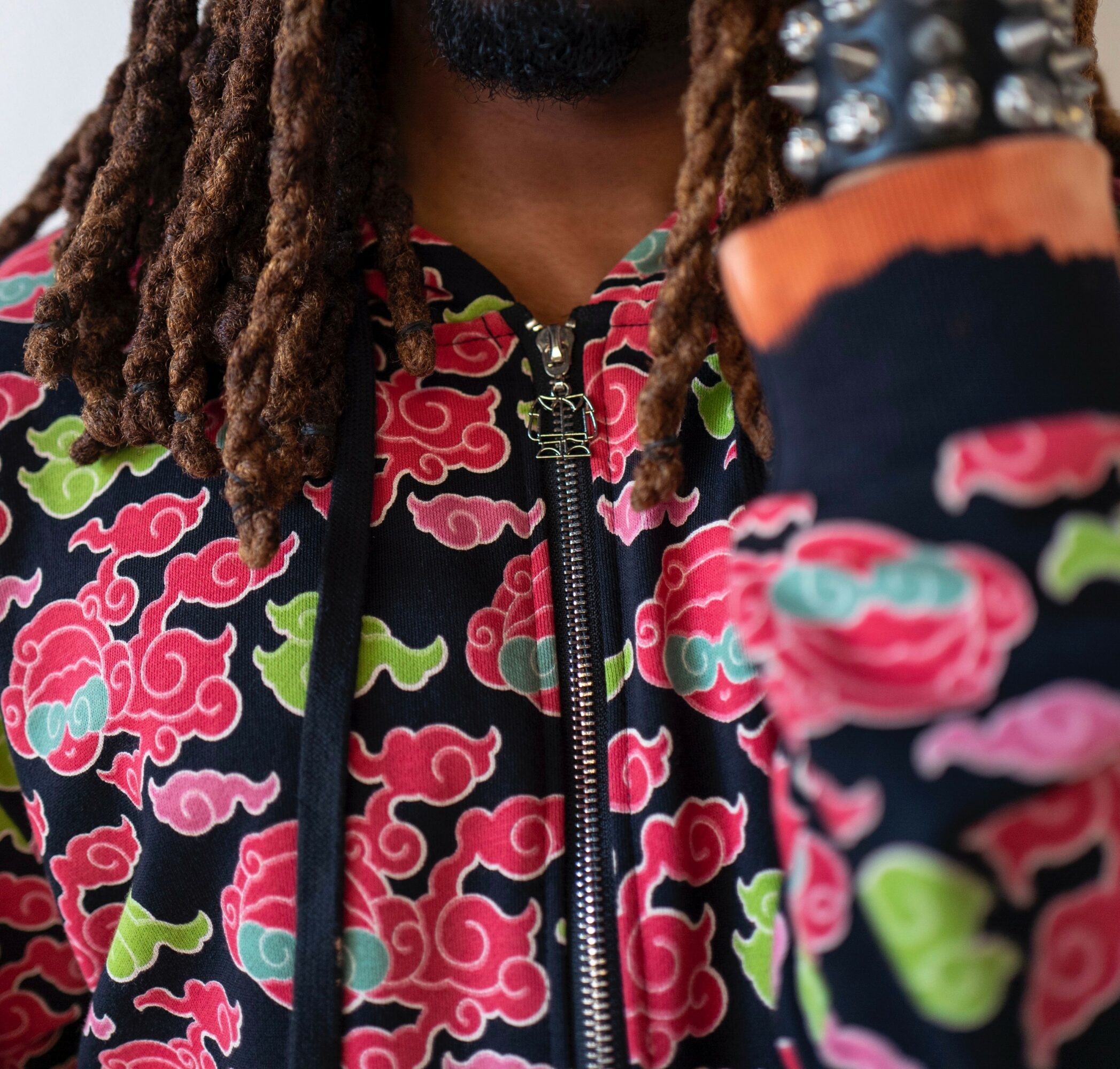 Close-up of a person wearing a colorful patterned jacket with a zipper, showing part of their face and dreadlocks.