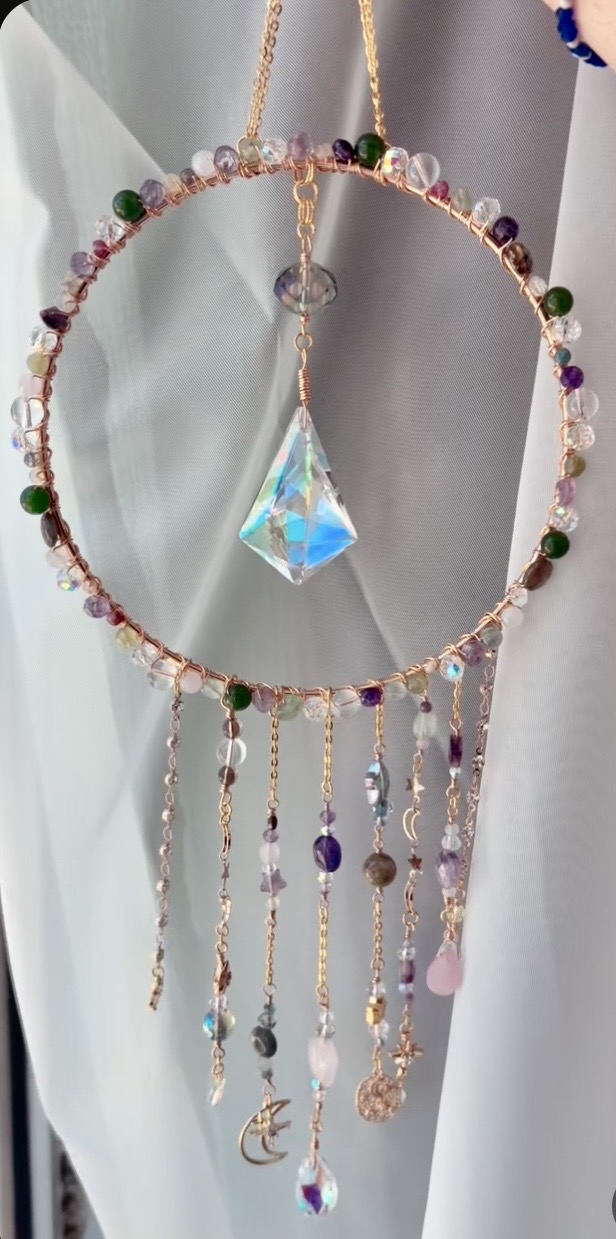 Decorative hanging ornament with beads, a large iridescent crystal, and dangling charms, against a light background.