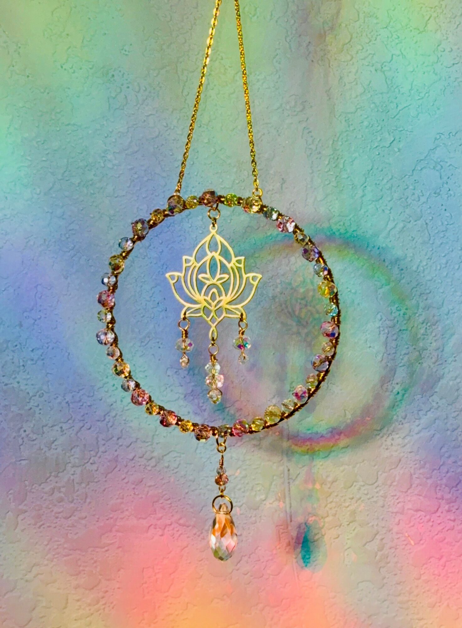 Hanging decorative ornament with a circular frame, a lotus-shaped centerpiece, and dangling crystals, against a colorful background.
