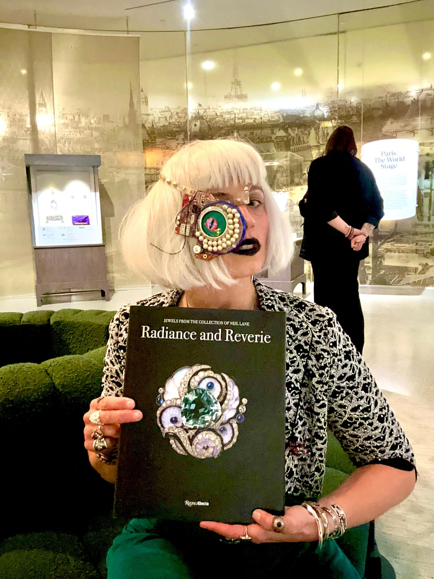 Person with white hair holding a book titled 'Radiance and Reverie' in a modern indoor setting.