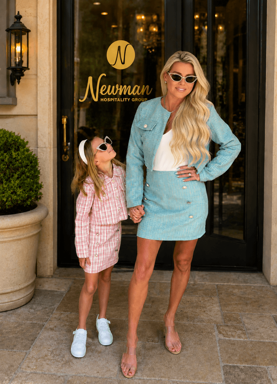 Woman and girl holding hands outside a building with glass doors, woman wearing sunglasses and a blue outfit, girl in pink checkered dress.