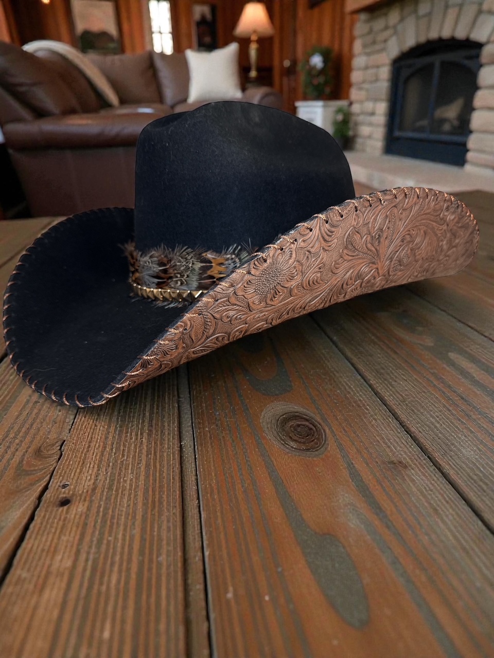 Black hat with a decorative band, placed on a wooden table in a cozy living room.