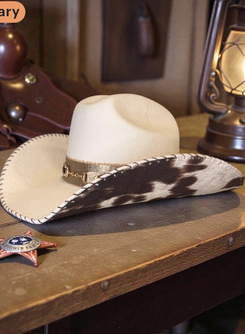 Cowboy hat with a wide brim and decorative band, placed on a wooden surface next to a sheriff's badge, in a rustic setting.