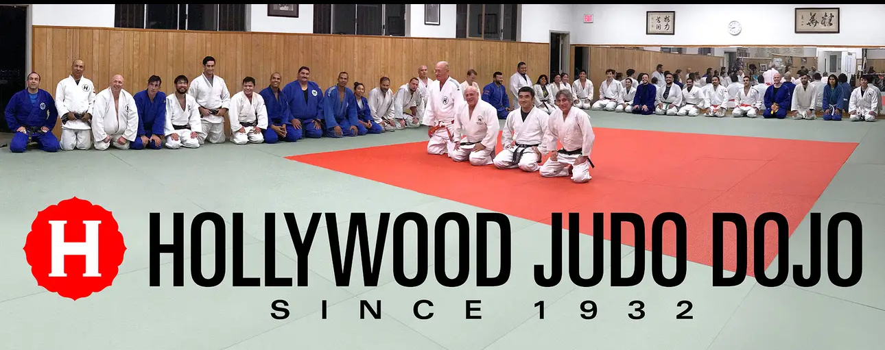Group of judo practitioners sitting on mats in a dojo, with text about Hollywood Judo Dojo since 1932.