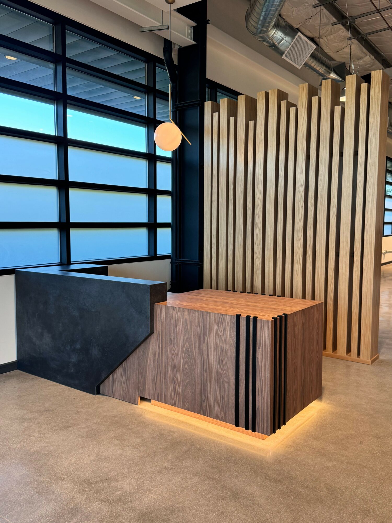 Interior space with large window, wooden slat wall, and a wooden table with a dark base, beige carpeted floor.