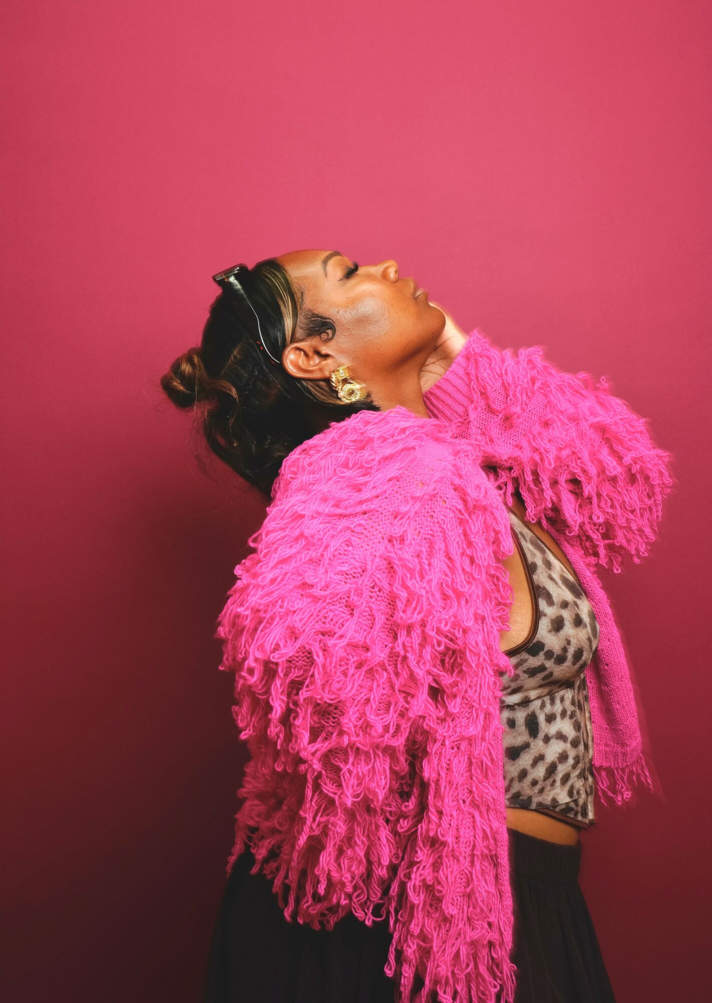 Woman with head tilted back, wearing a pink fluffy jacket and leopard print top, against a pink background.