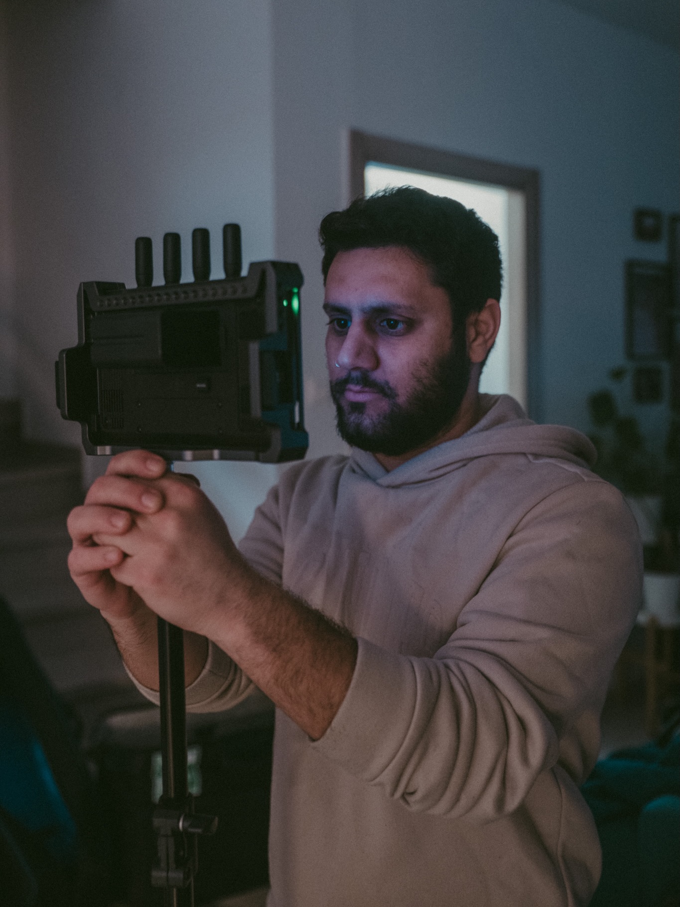 Man with dark hair and beard operating a camera on a tripod indoors, focused on filming.