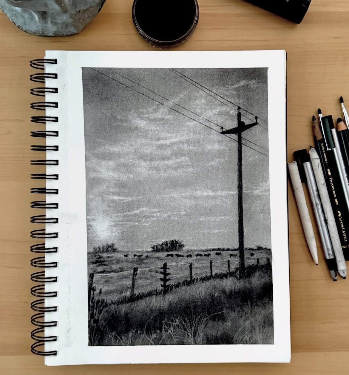 Black and white photo of a rural landscape with a power pole, fence, and cloudy sky.