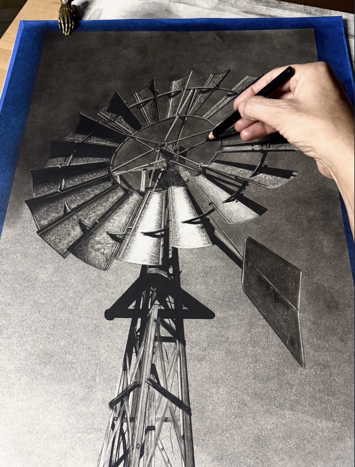 Person drawing a windmill diagram on a blackboard with a marker, windmill's blades and tower visible.