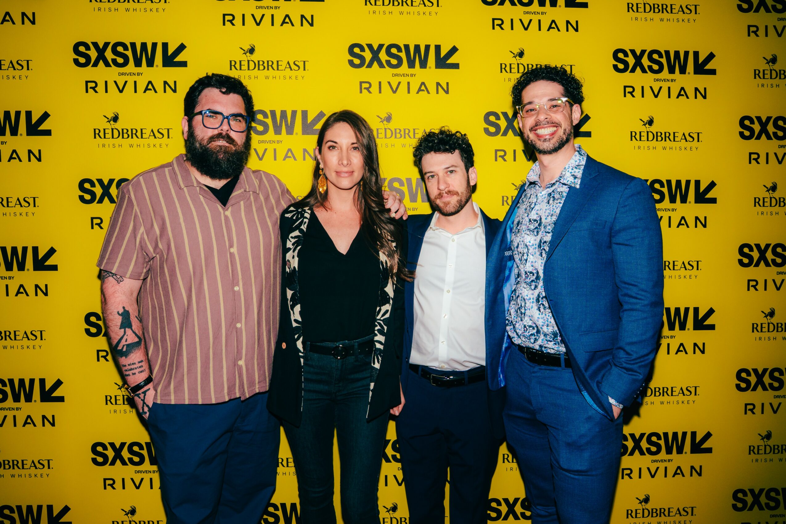 Four people standing in front of a yellow SXSW backdrop, smiling, dressed in casual and formal attire.