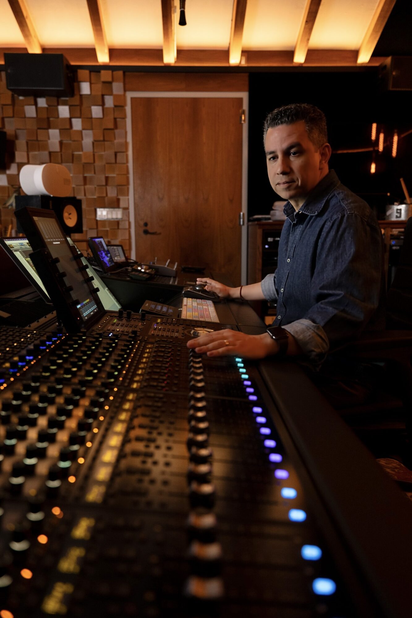 Person operating sound mixing console in a dimly lit room with wooden ceiling beams.