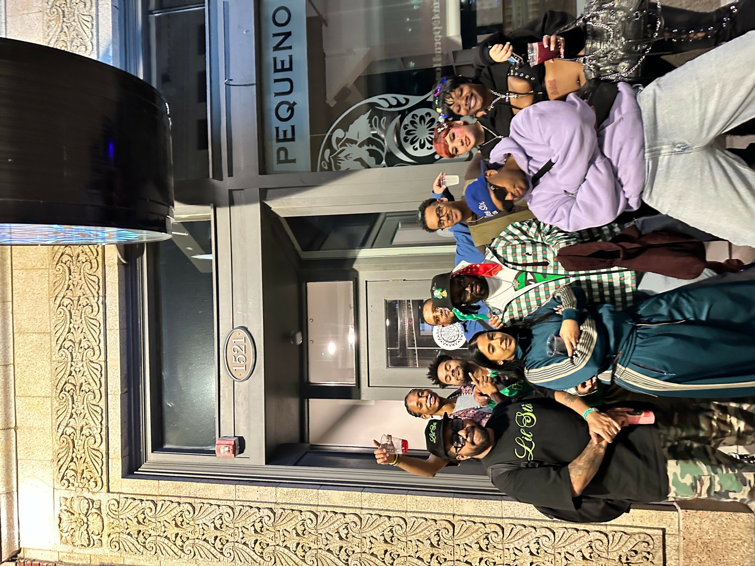 Group of people standing outside a building with glass doors, some holding drinks, smiling, and posing for the photo.