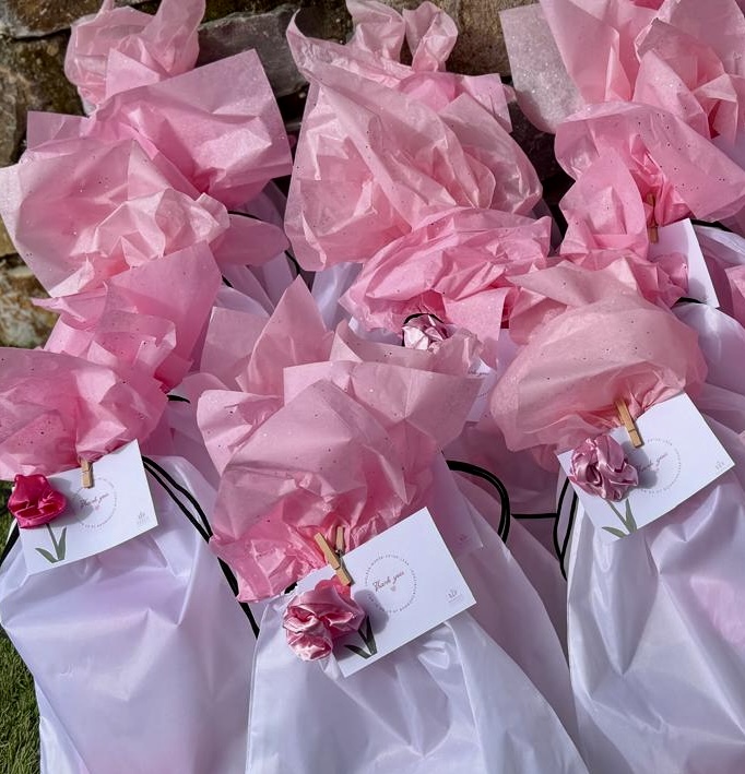 Multiple pink and white gift bags with tissue paper and small decorative flowers, arranged outdoors.