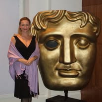 Woman standing next to a large gold-colored sculpture of a face with stylized hair, in an indoor setting.