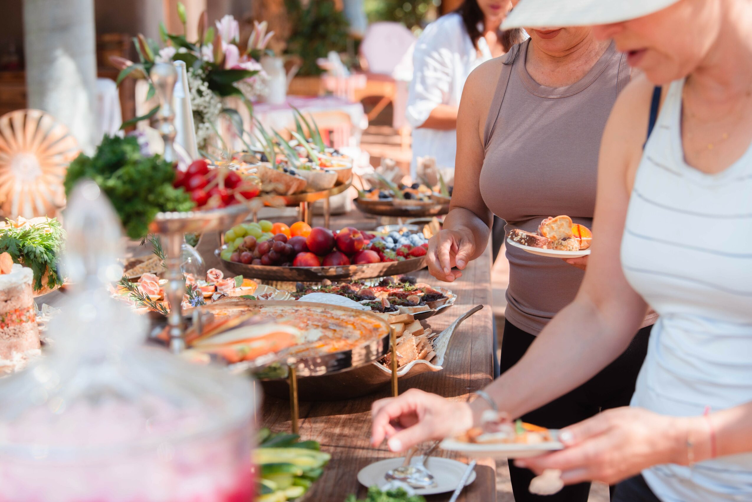 People at an outdoor buffet table with desserts and flowers, serving themselves and selecting treats.