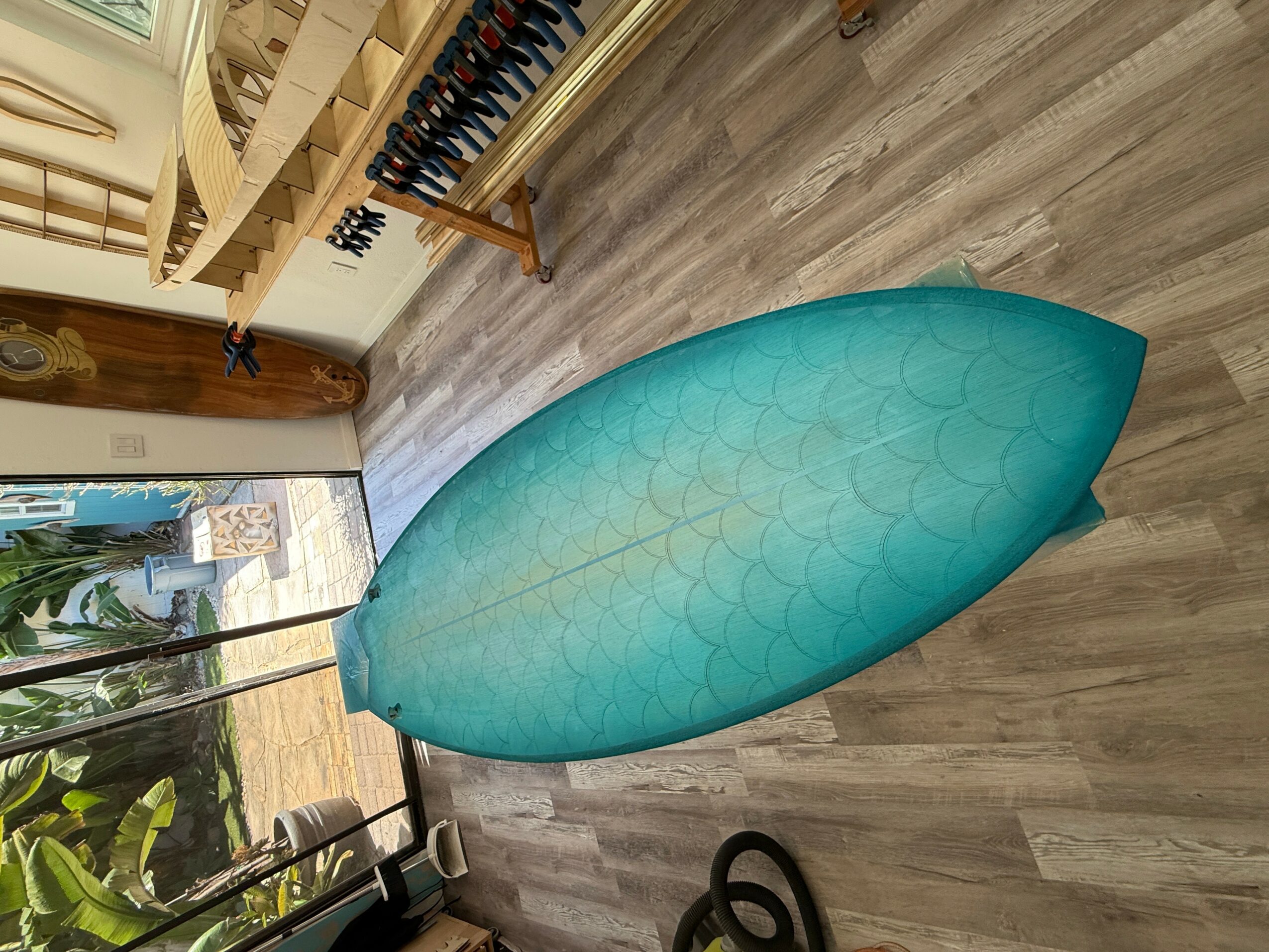 A turquoise ironing board with a patterned surface stands on a wooden floor inside a room.