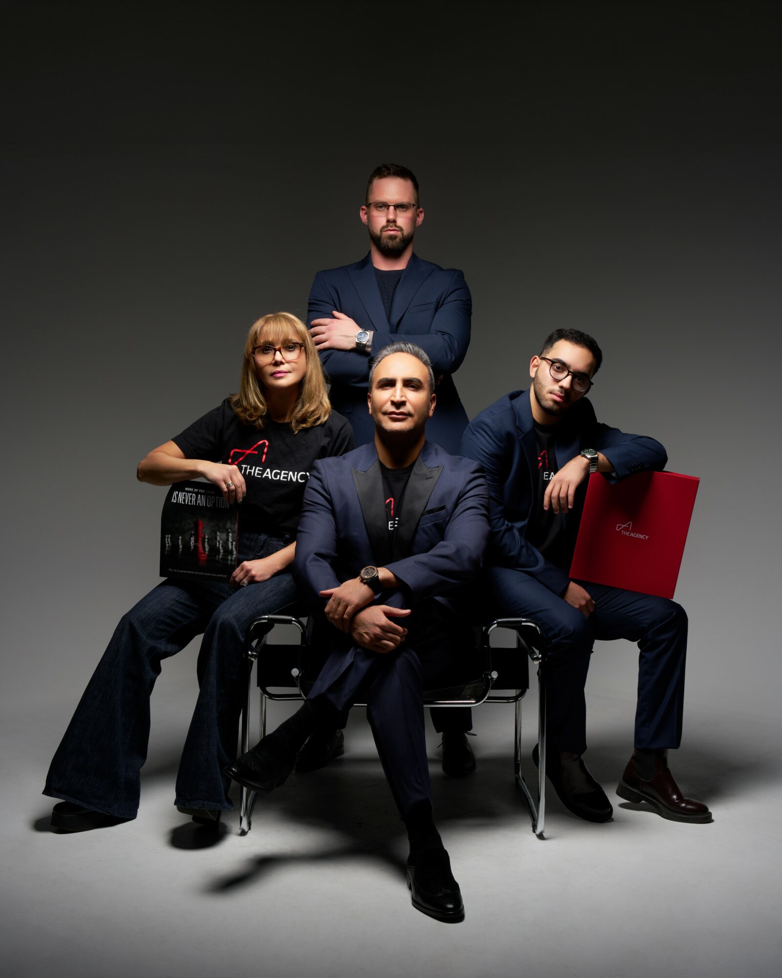 Group of four people, three sitting and one standing, in a studio with a dark background.