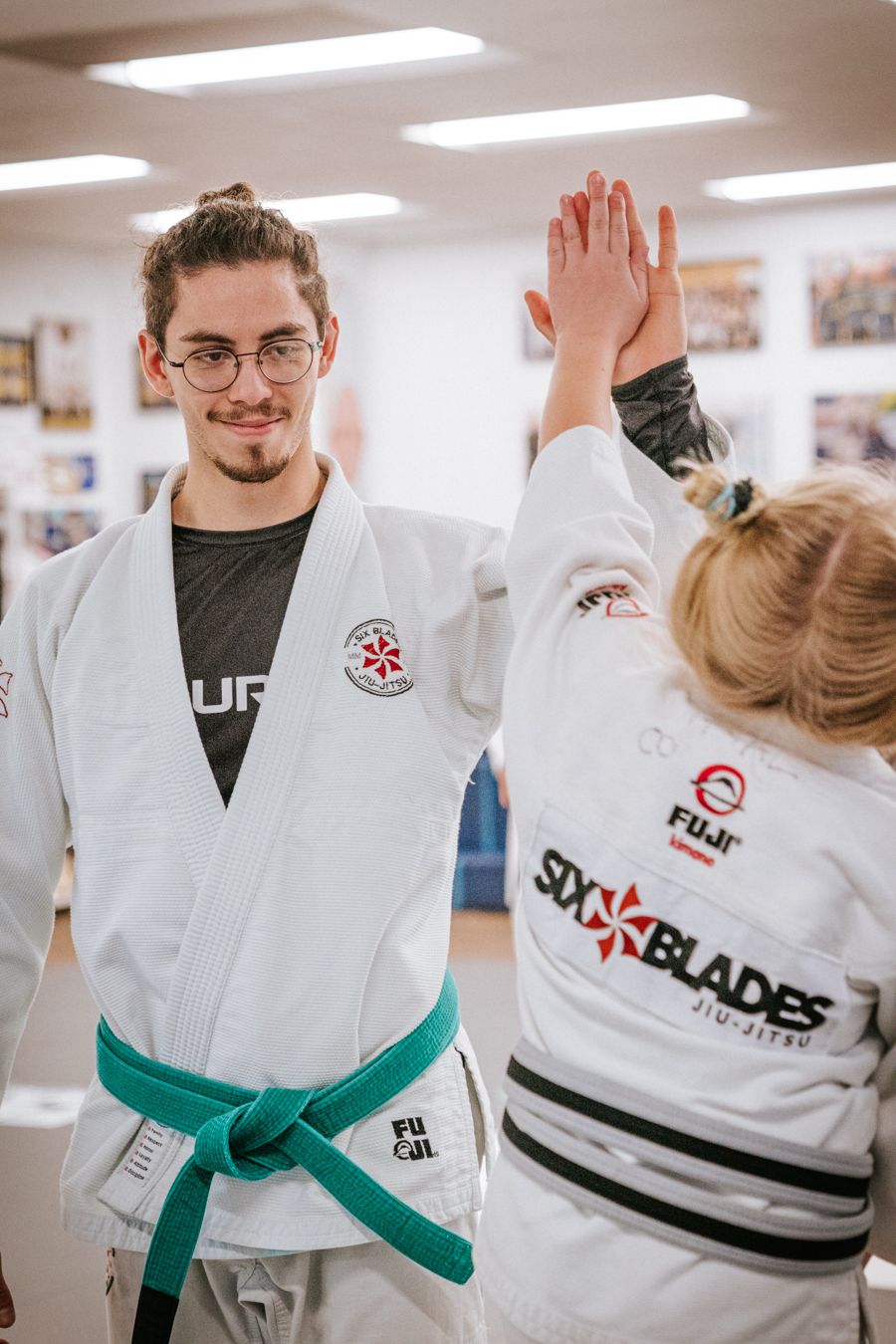 Person in a martial arts uniform giving a high five to another person in a martial arts uniform, in a training room.