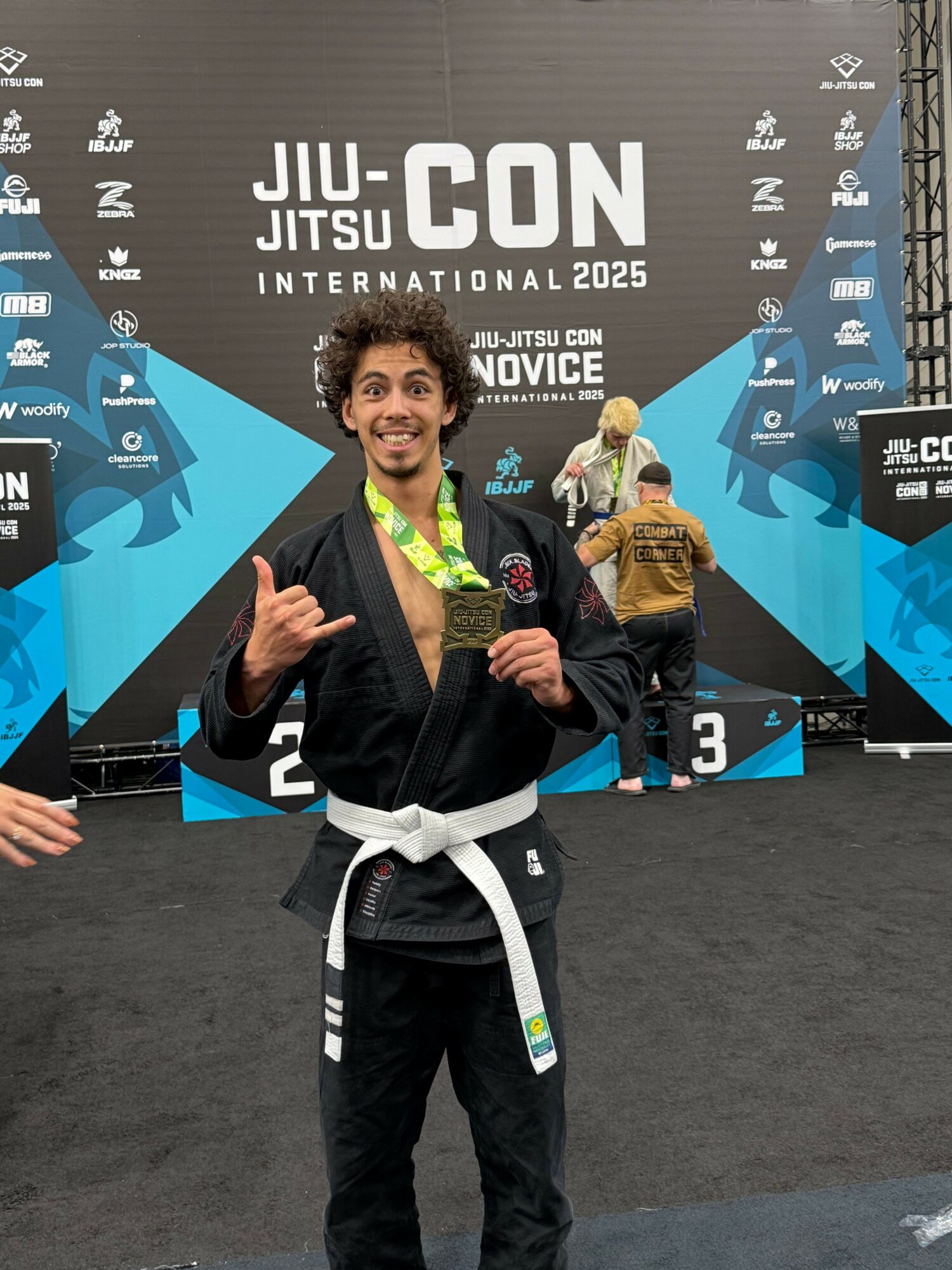 Person in a black gi with a white belt holding a trophy, standing on a podium at a martial arts event.