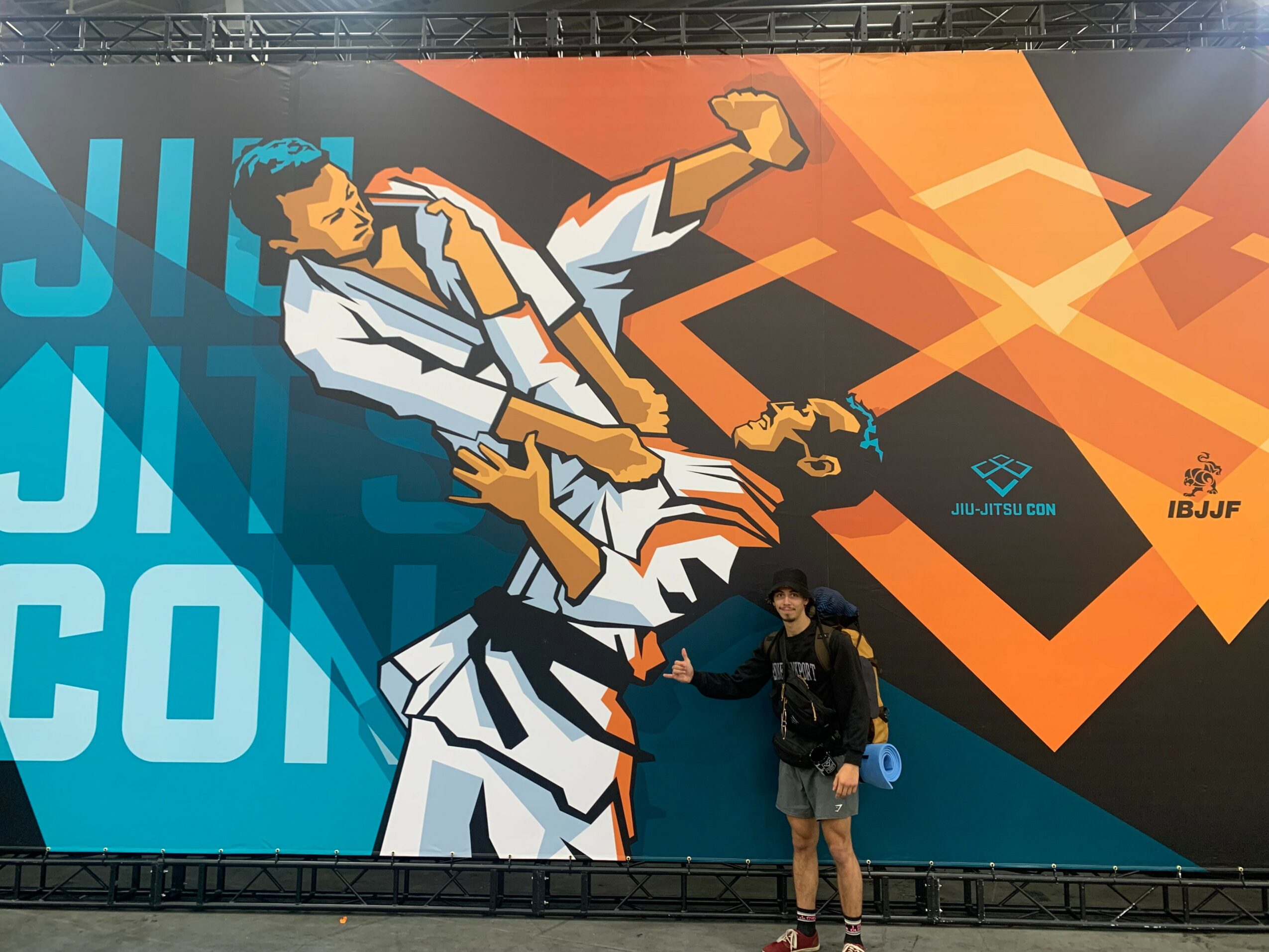 Person standing in front of a large colorful mural of two martial artists in a fighting stance, with abstract shapes and logos.