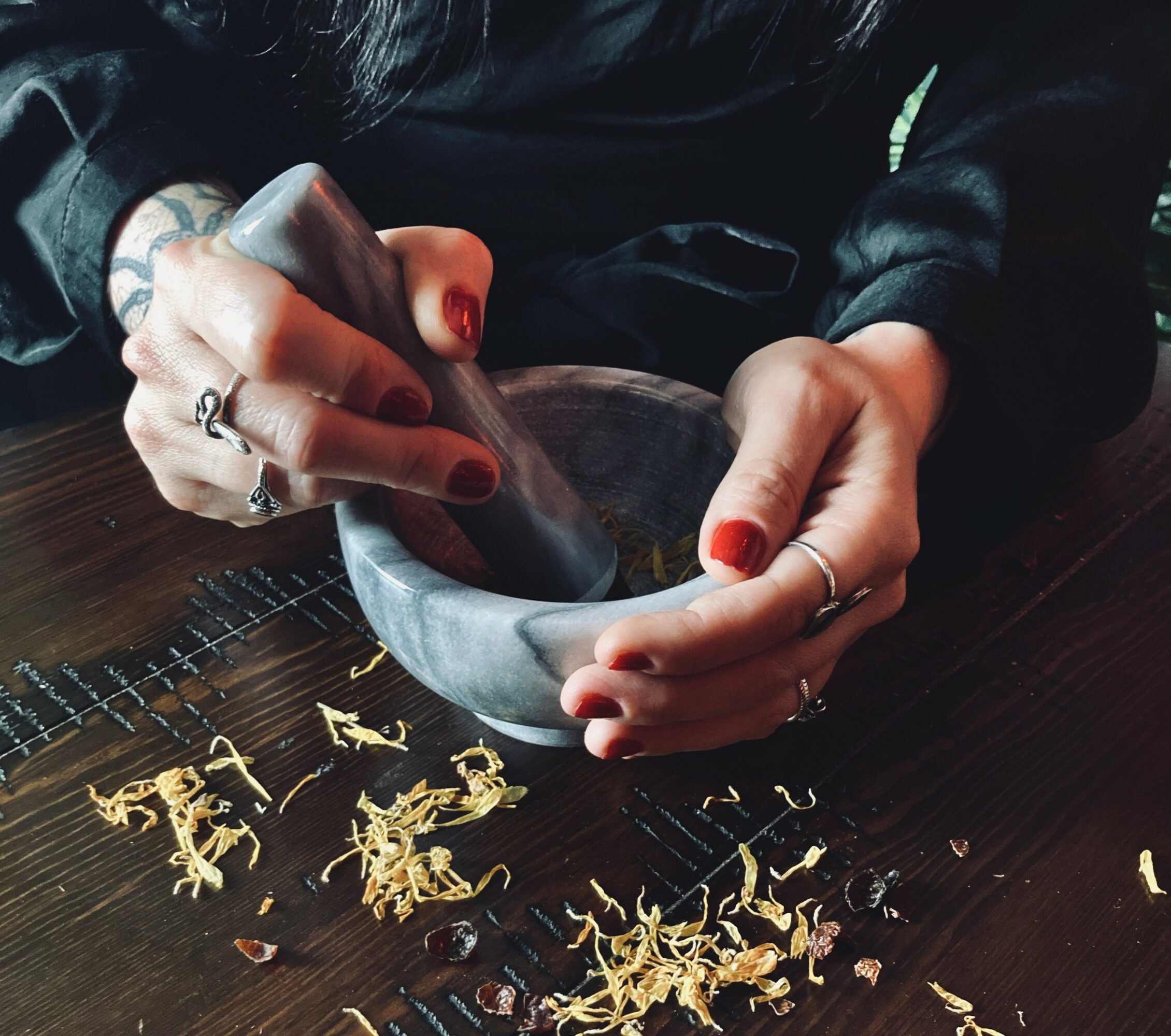 Person grinding spices with a mortar and pestle, with spice shavings on a dark wooden surface.