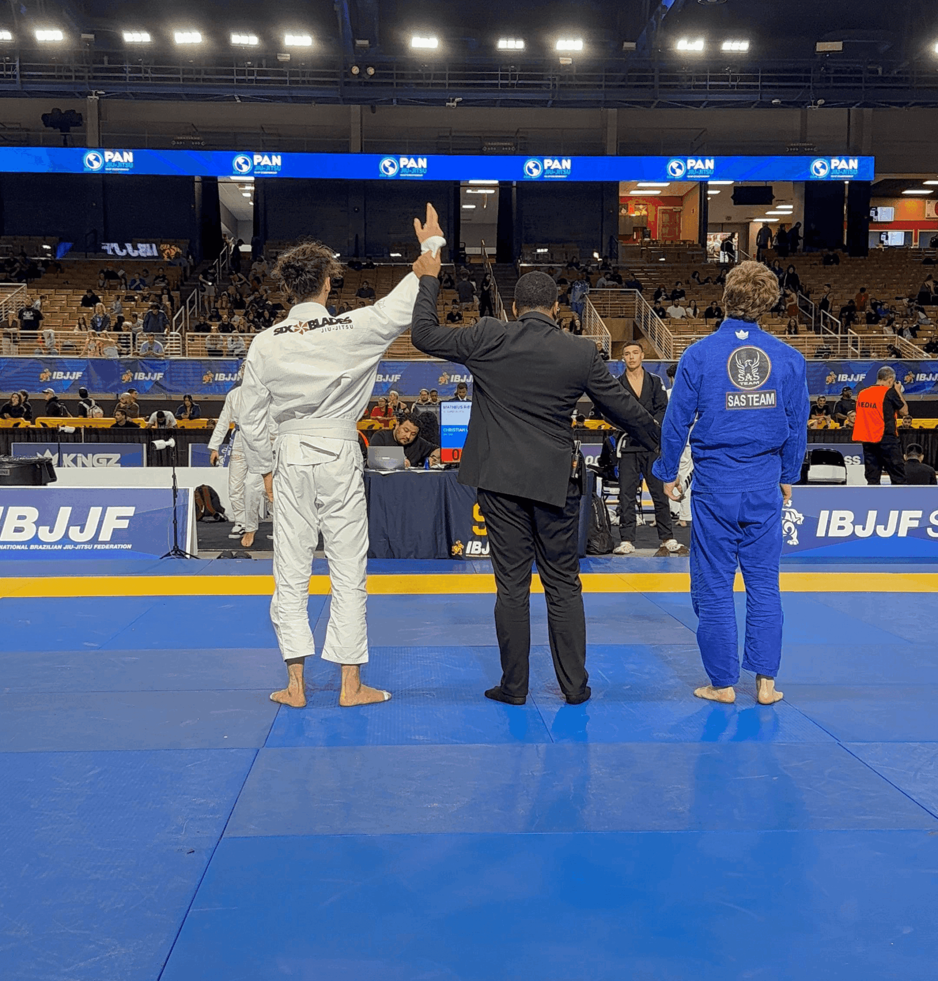 Two judo competitors and a referee in a sports arena, one competitor in white, the other in blue, with referee raising hand.