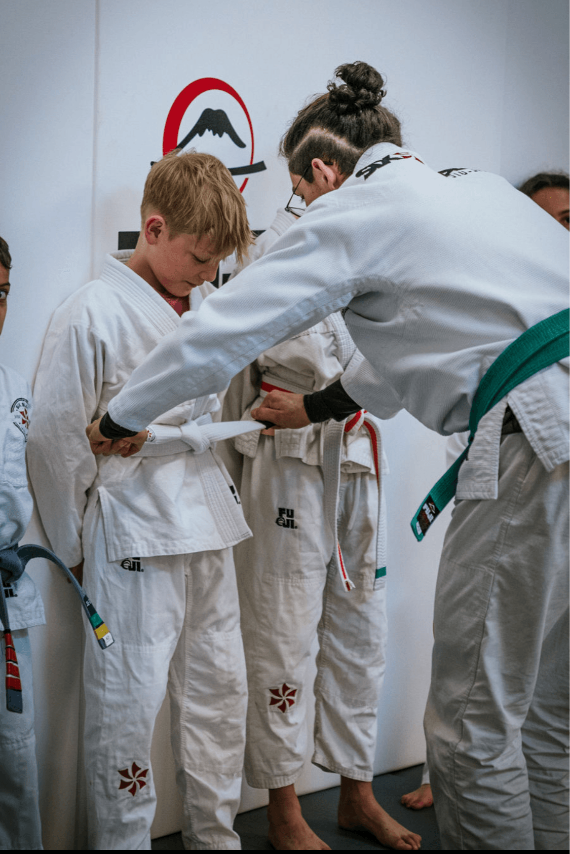 Martial arts instructor awards a medal to a young student in a gi, with other students in gi in the background.